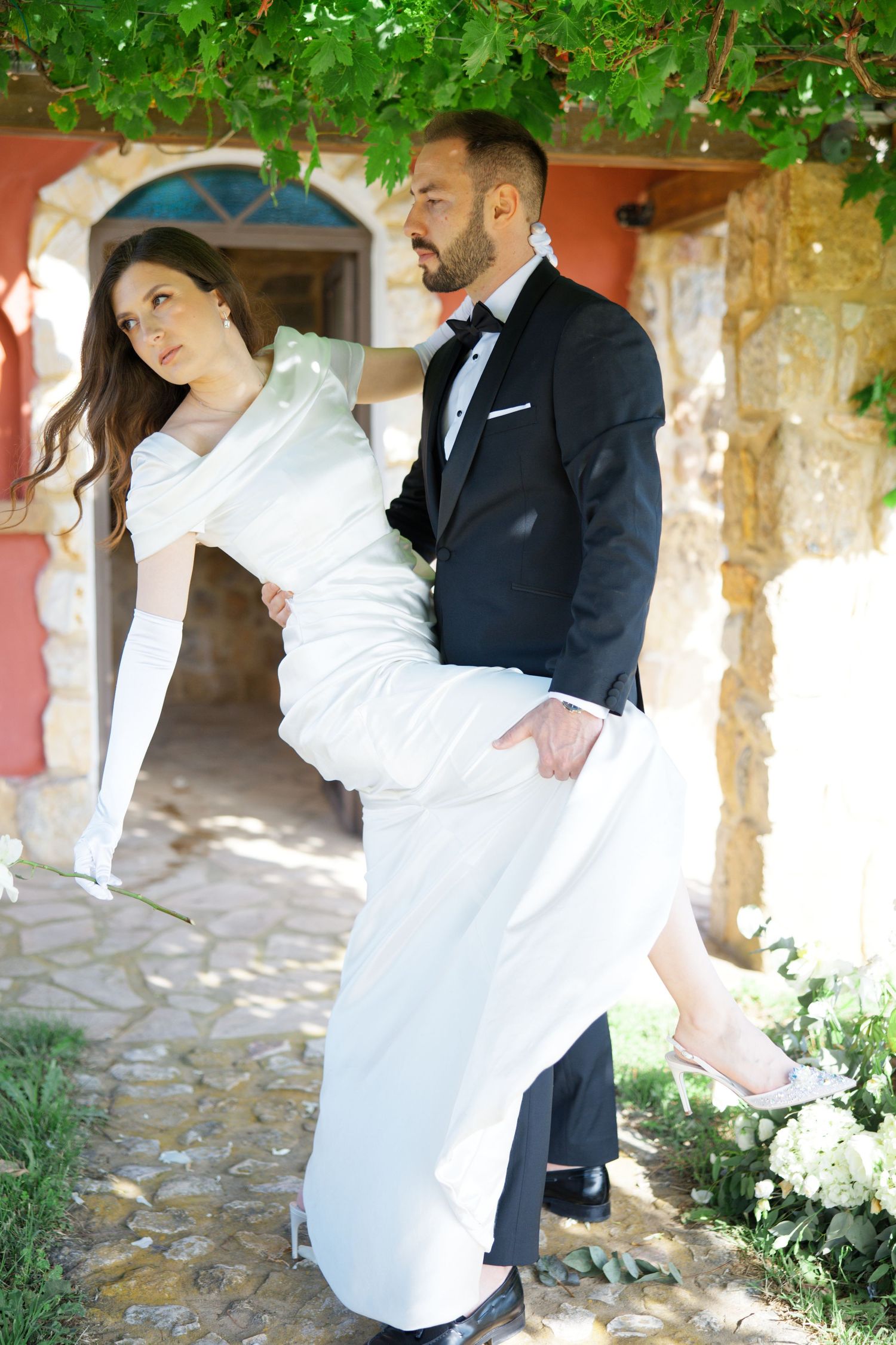 Playful wedding photo series in front of stone architecture with greenery.