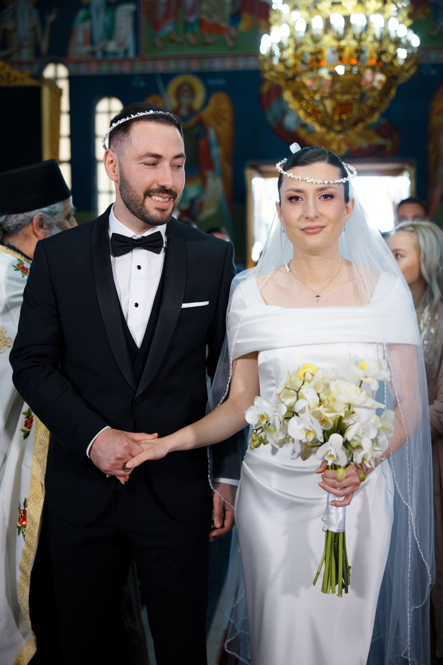 Elegant church wedding ceremony with bride in white gown holding bouquet next to groom in black tuxedo.
