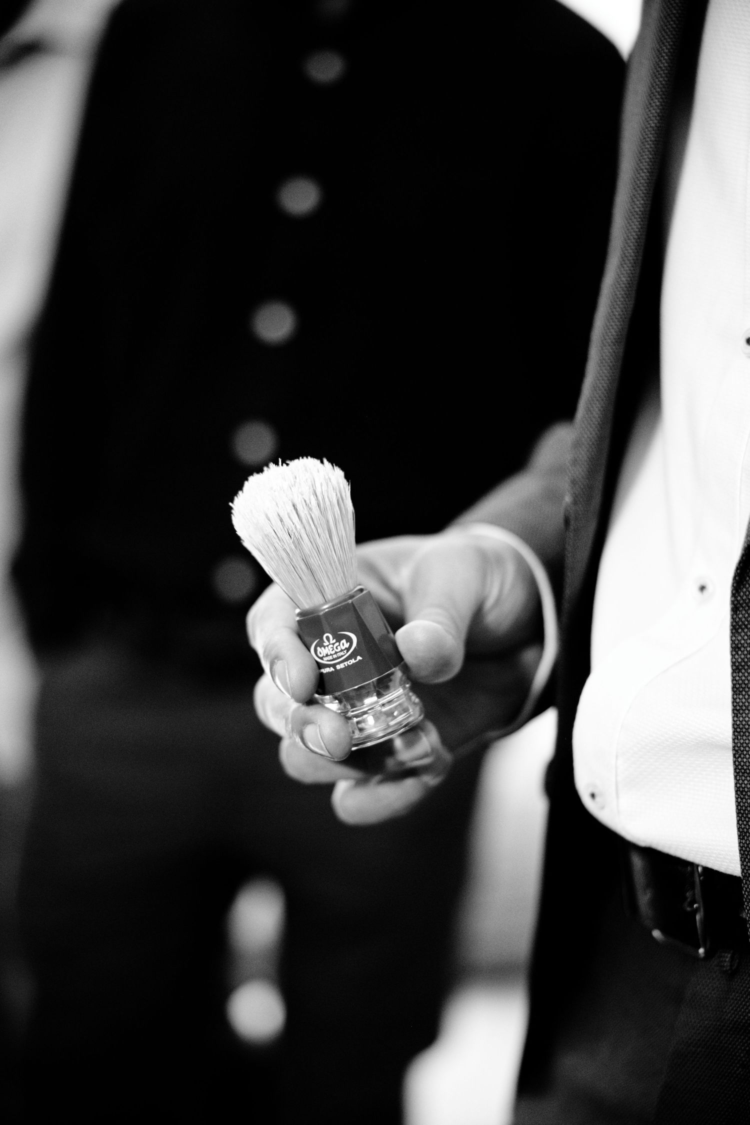 Close-up black and white shot of a shaving brush being held during wedding preparation.