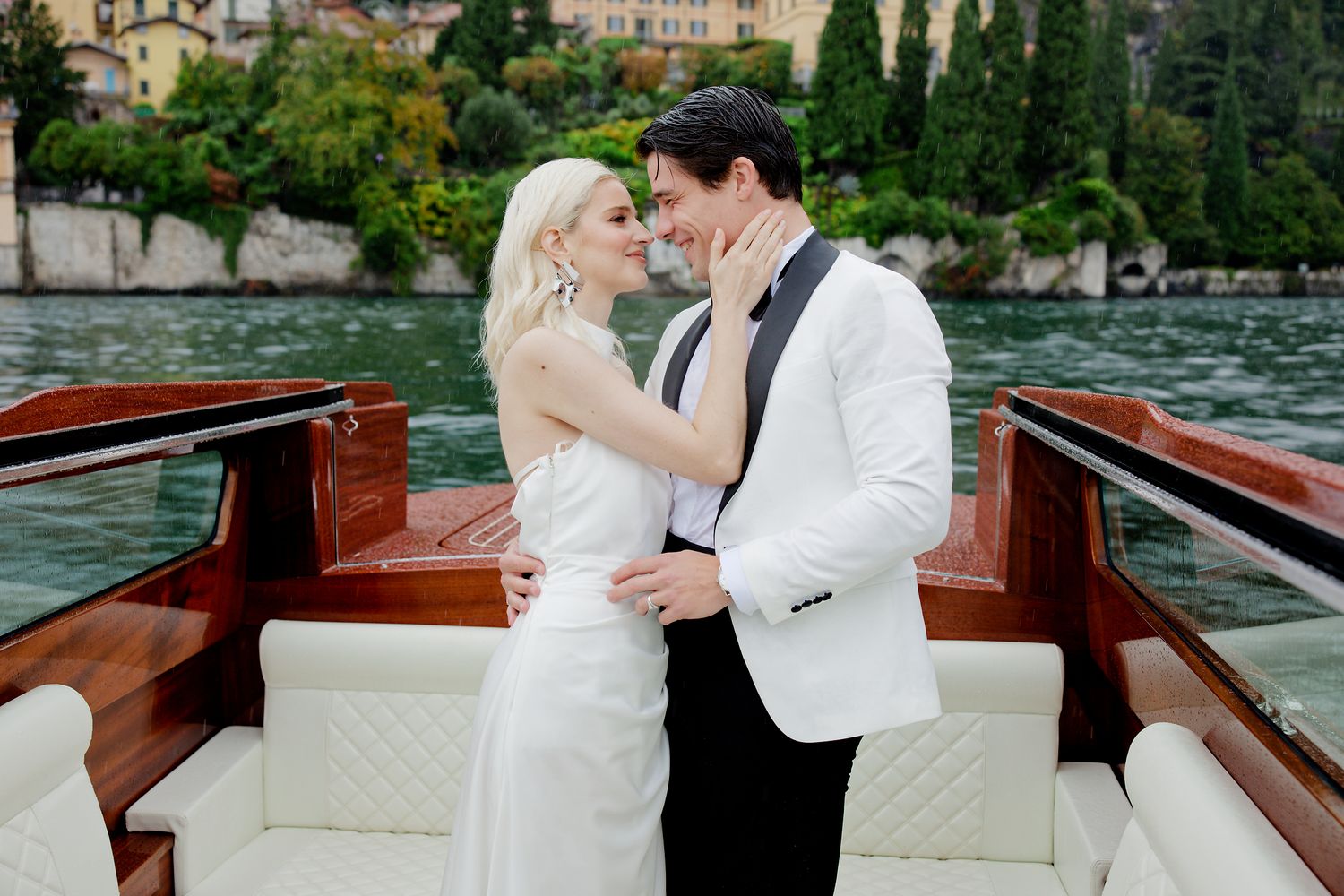 Newlyweds share romantic moment on luxury wooden boat in scenic lake setting.