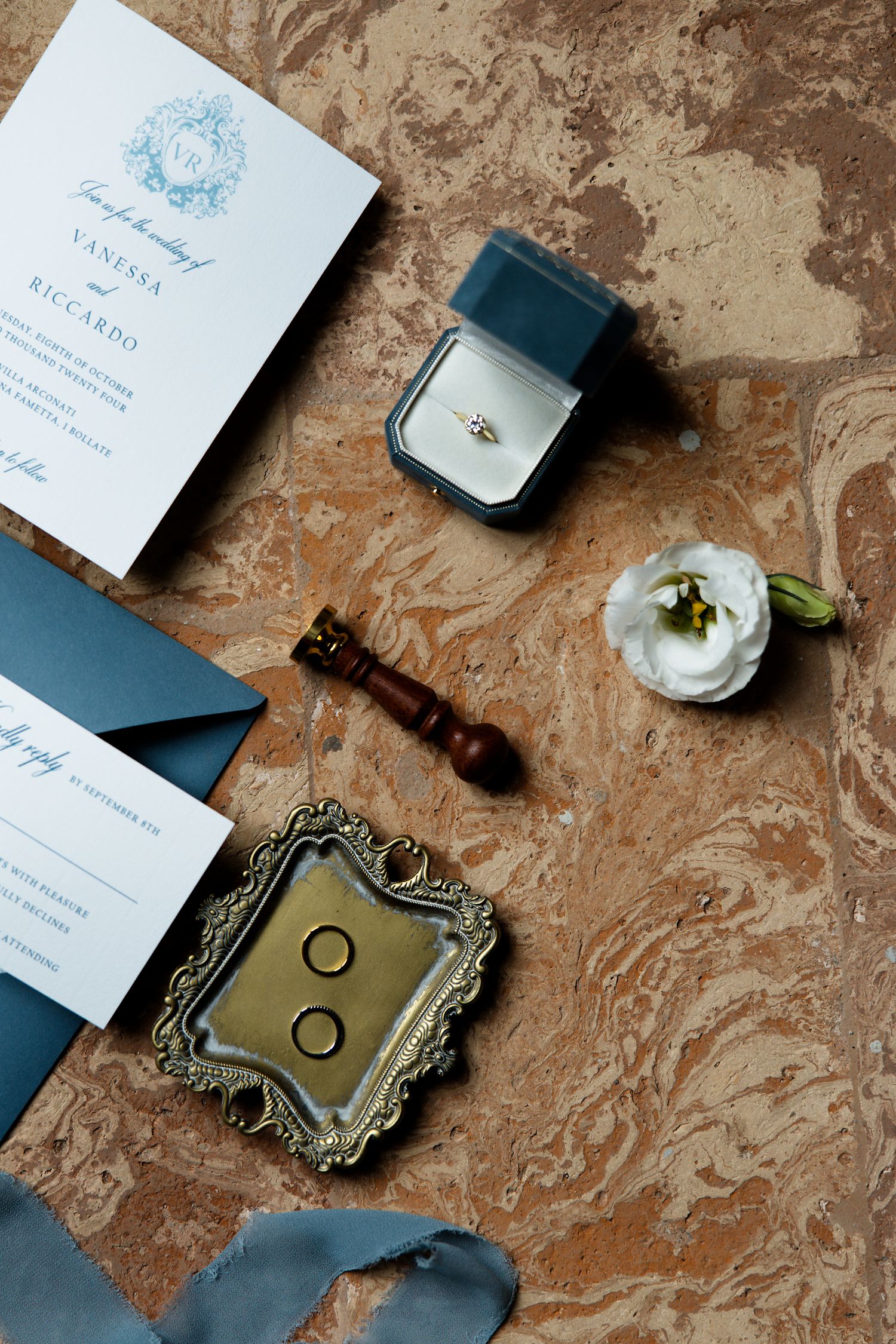 Wedding details flatlay with blue stationery, ring box, white flower and vintage accessories.