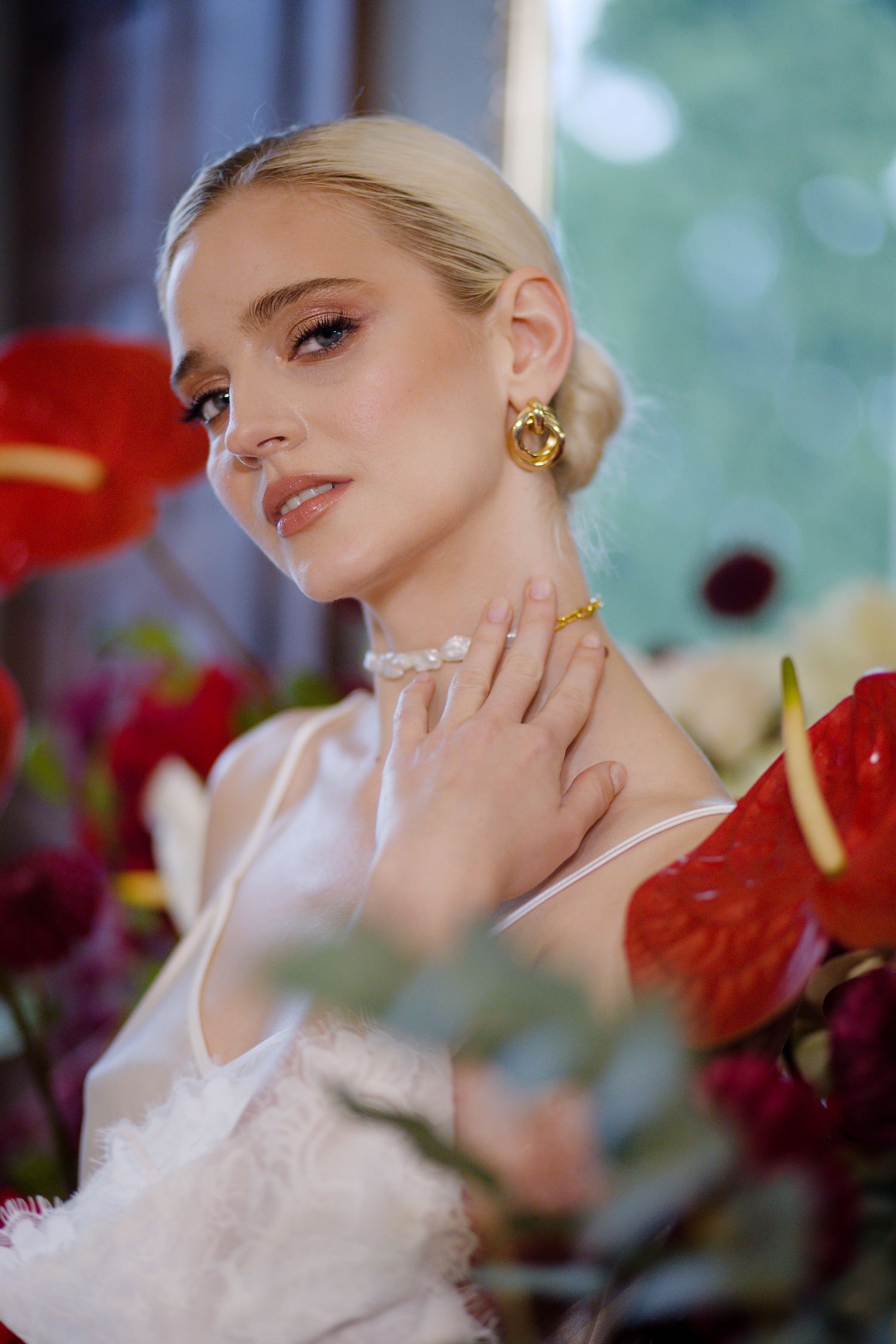 Close-up bridal portrait showcasing elegant makeup and gold jewelry among red anthurium flowers.