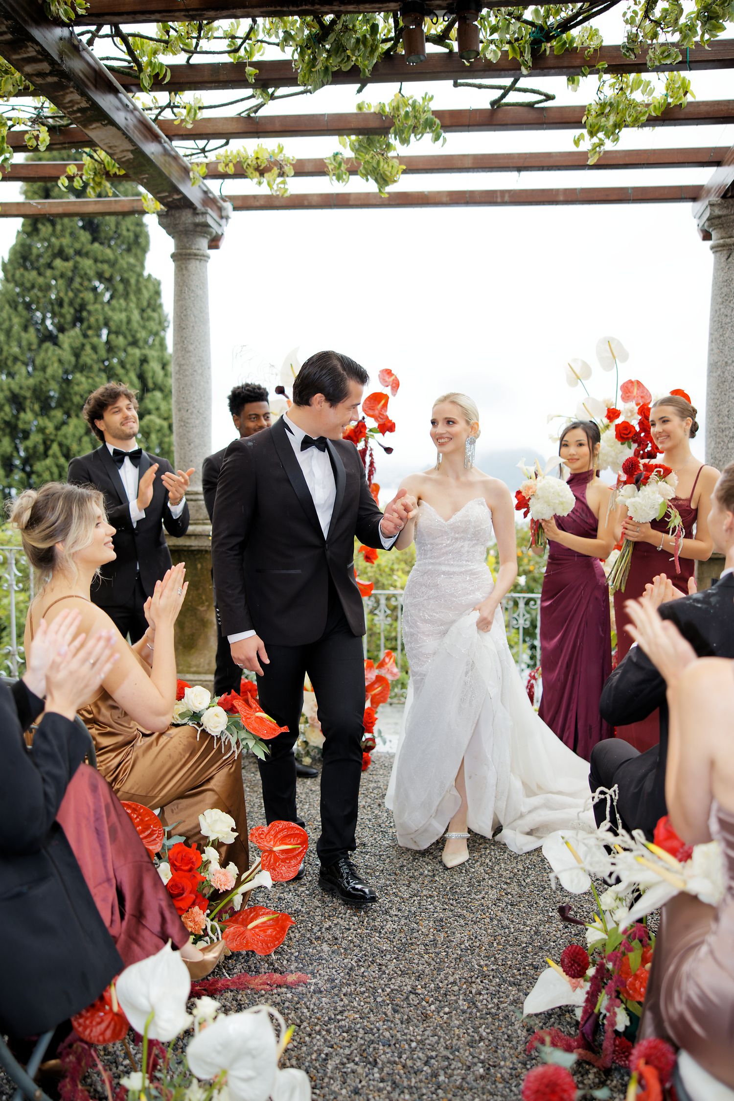 Wedding ceremony under a pergola decorated with red and white floral arrangements.