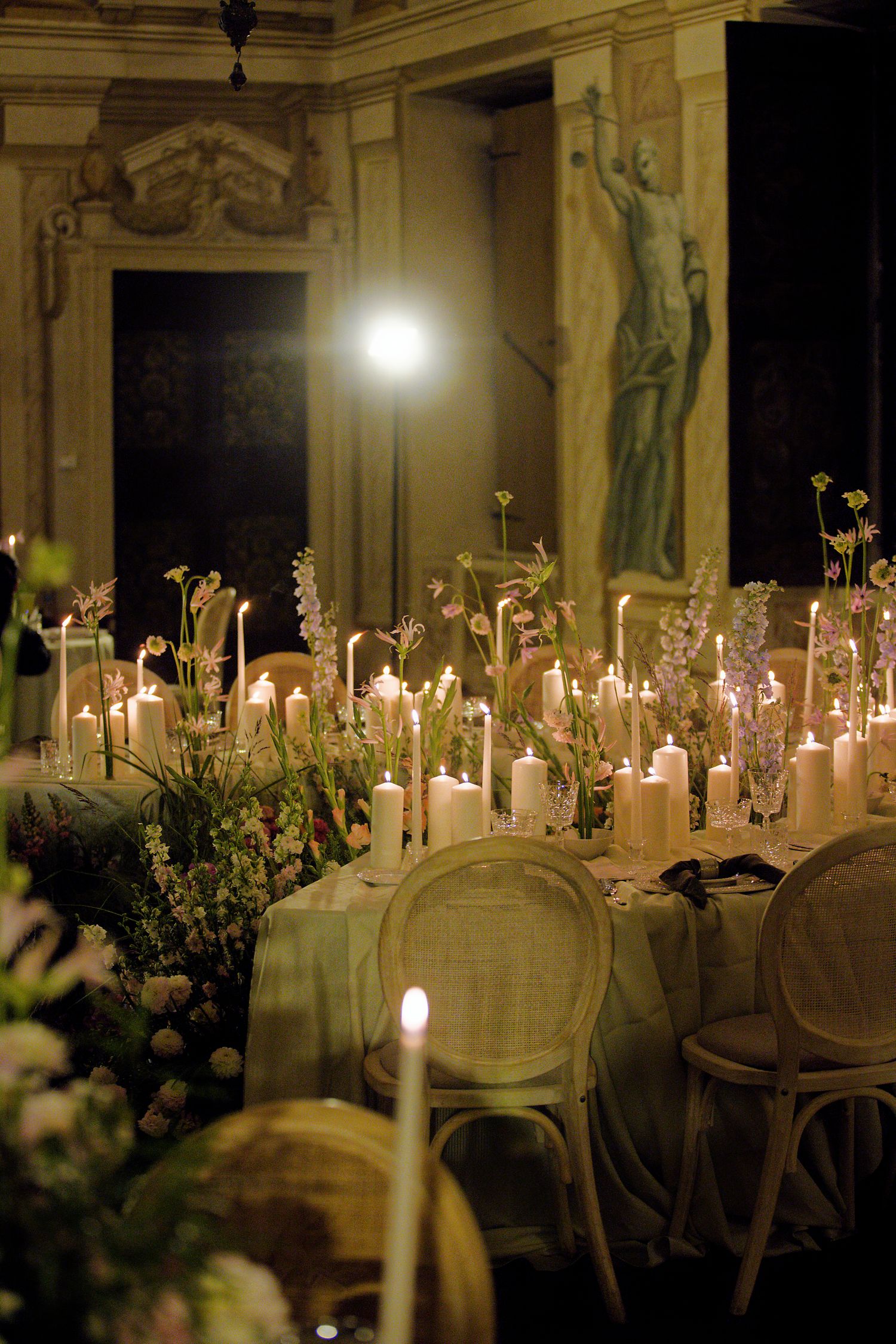 An elegant candlelit reception table with vintage chairs and floral arrangements in a grand Italian villa.