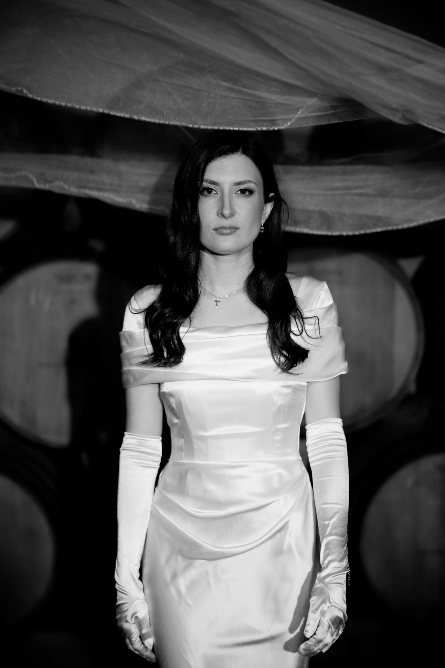 A bride poses in an elegant white satin wedding gown with long sleeves.