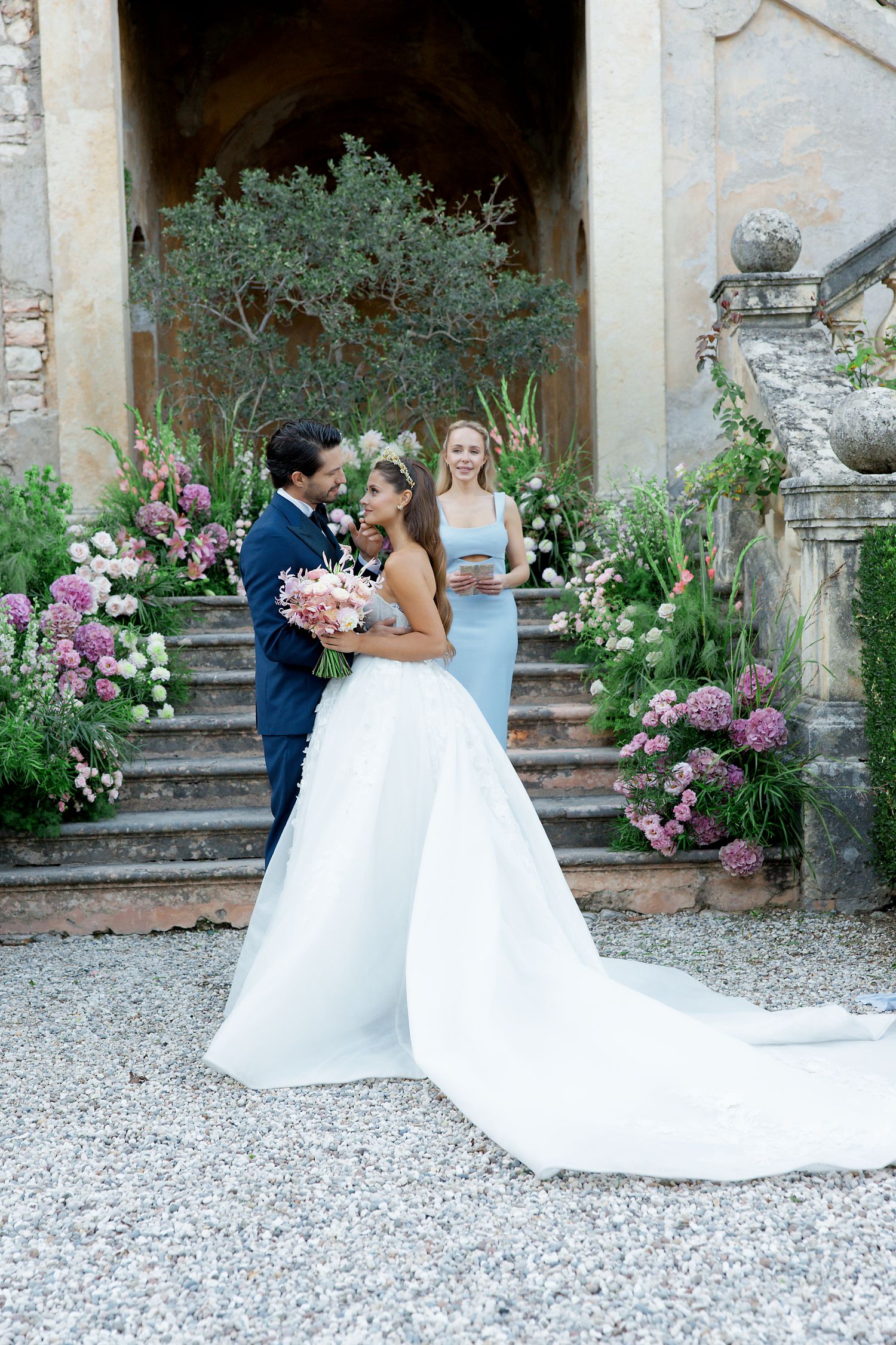 Wedding ceremony scene on stone steps adorned with pink flowers and greenery.