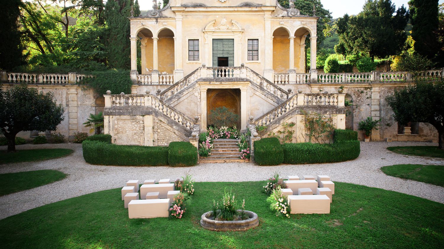 Elegant mansion with symmetrical stone staircase and outdoor lounge seating arranged on manicured lawn.