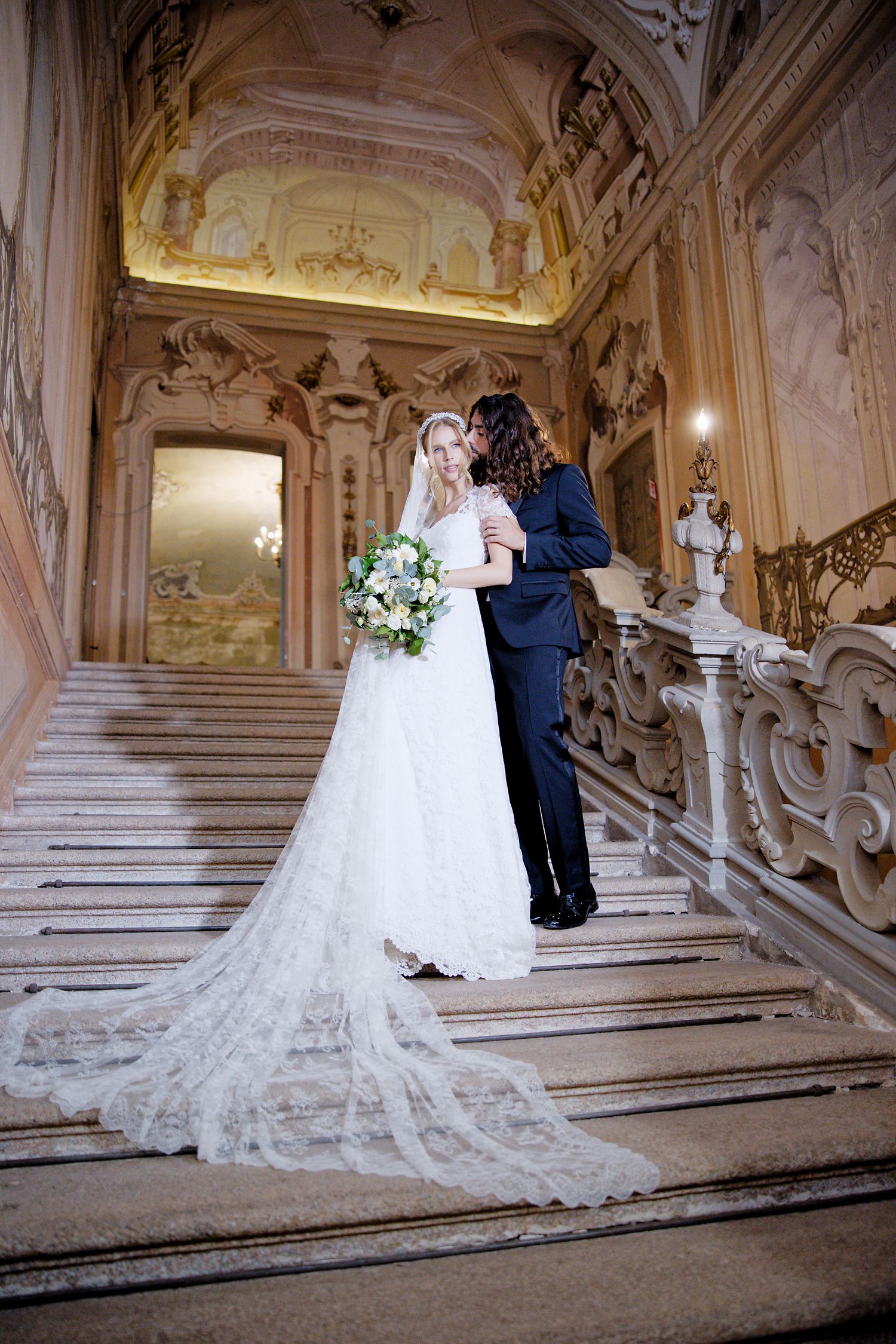 A romantic wedding moment captured on an ornate marble staircase with baroque details and decorative architecture.