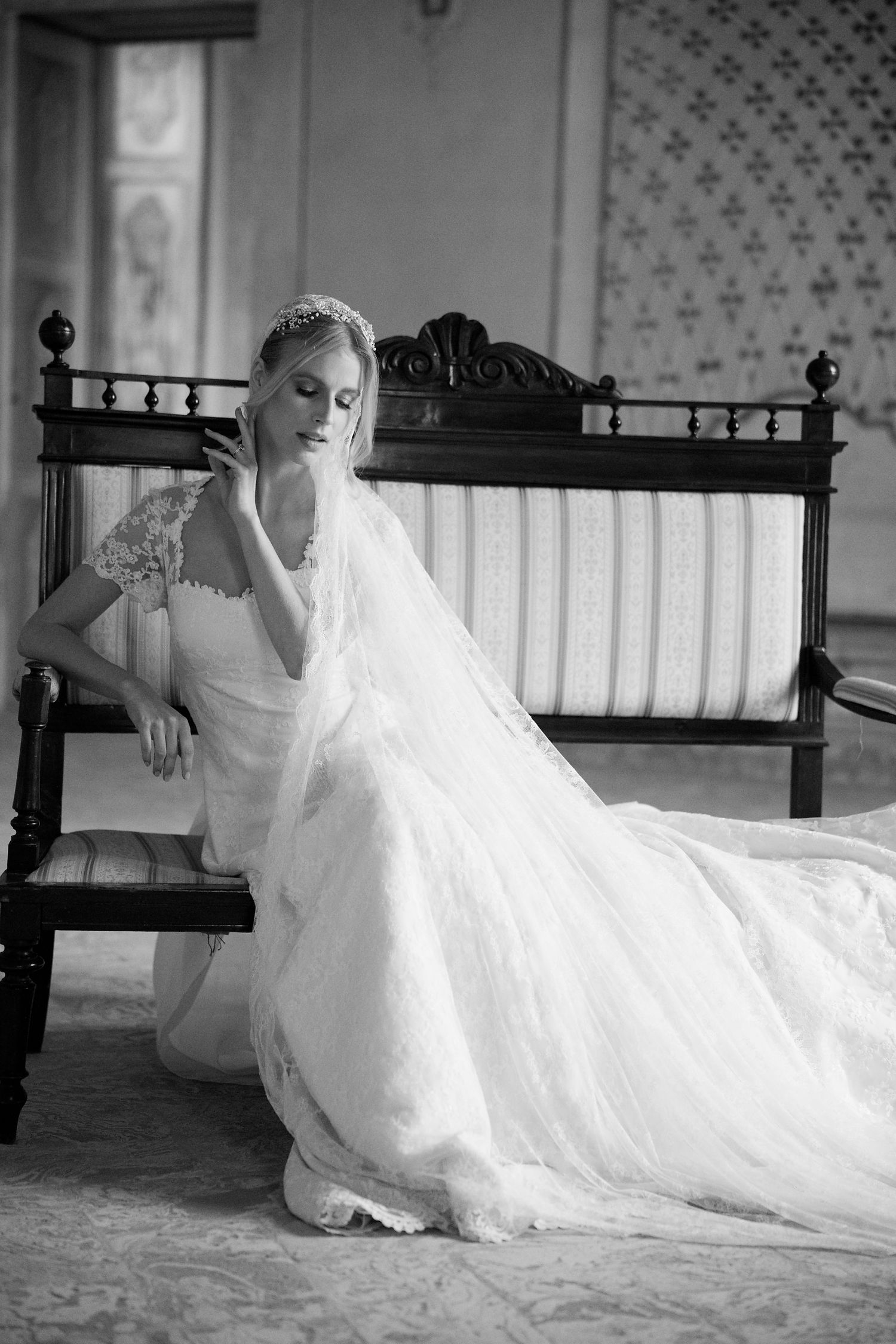 Classic black and white photo of bride reclining on antique bench with flowing dress train.
