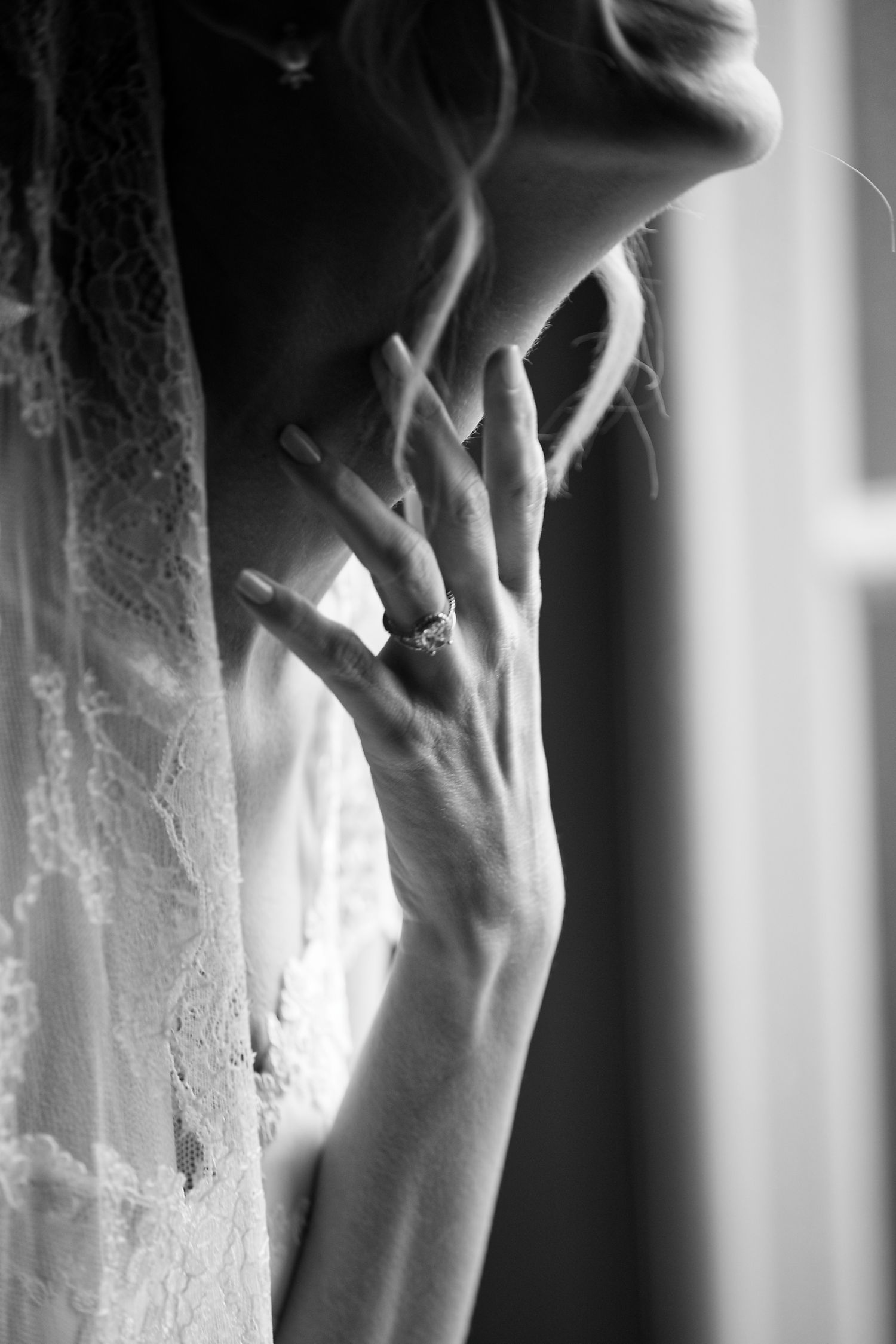 Black and white close-up of a hand with engagement ring held near face in soft window light.