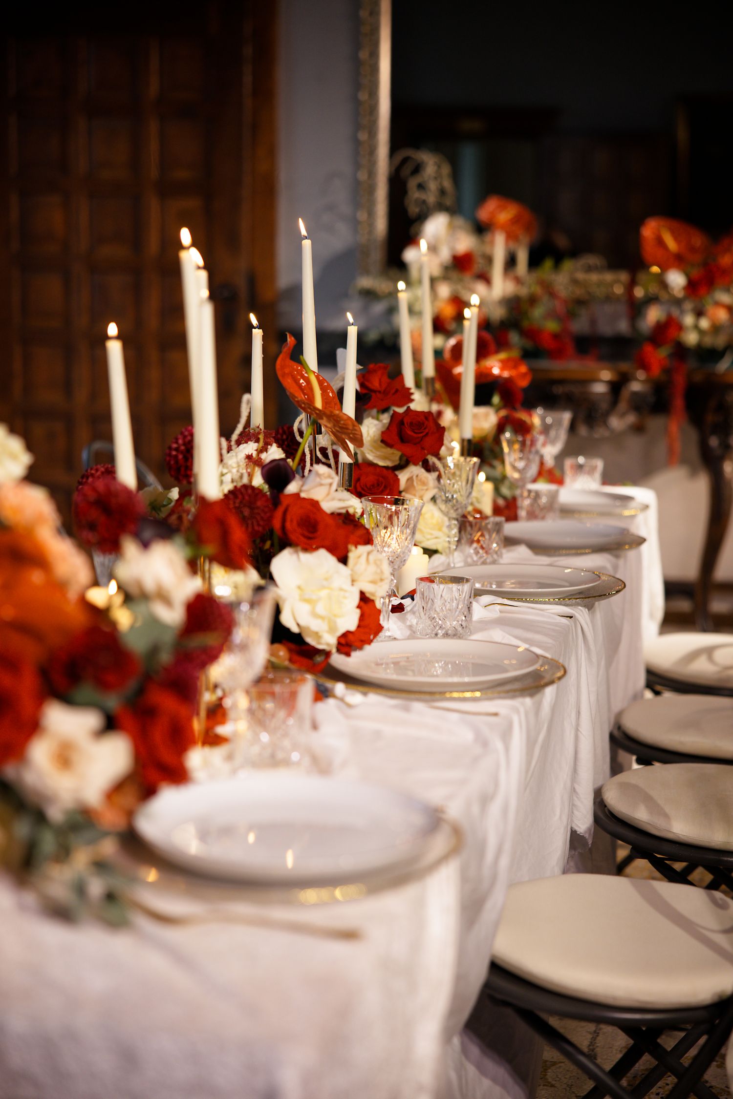 Elegant wedding table setting with red and white flowers, tall candles, and white linens.