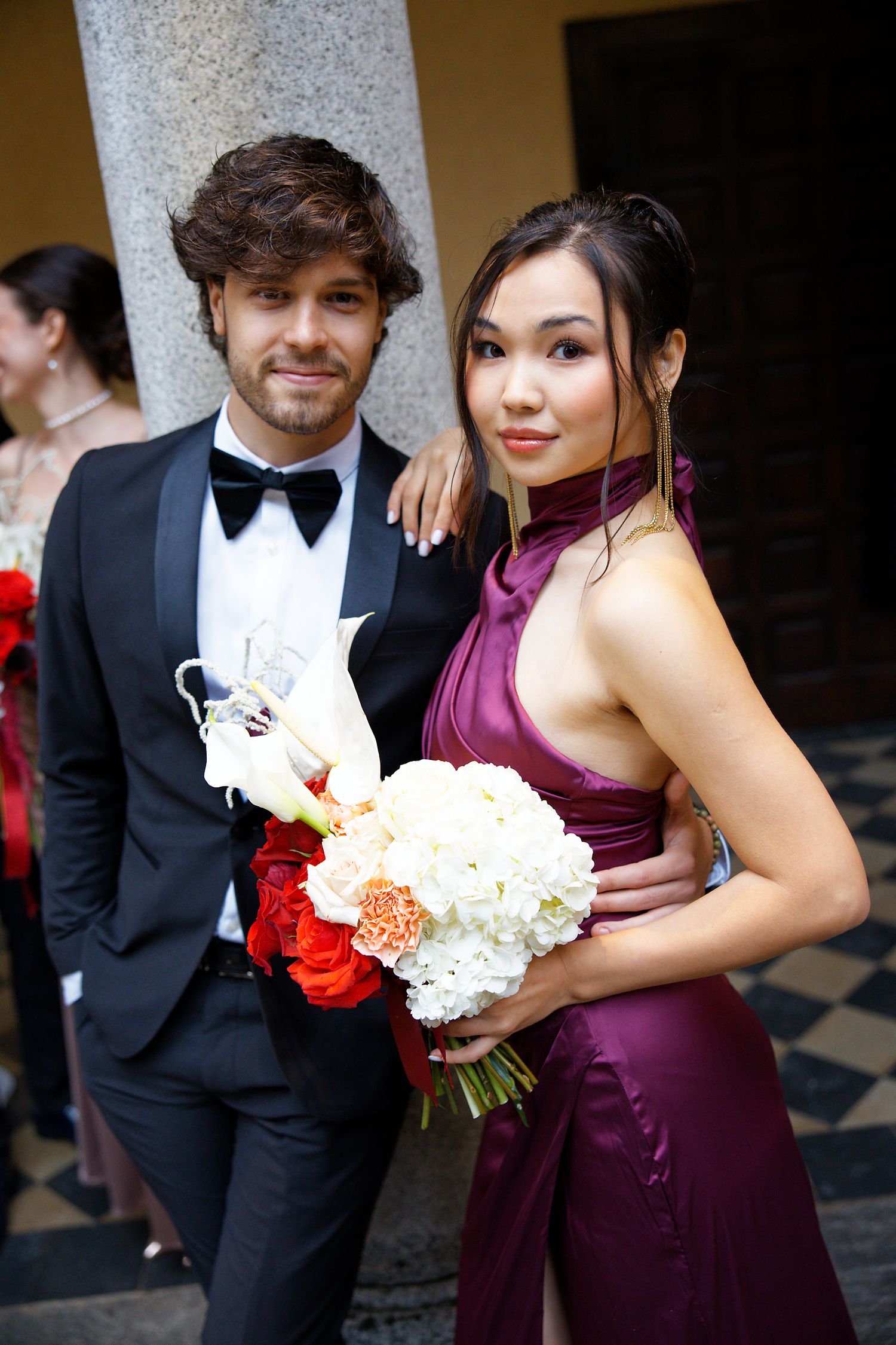 Wedding attendees in formal attire pose with bouquet of white and red flowers.