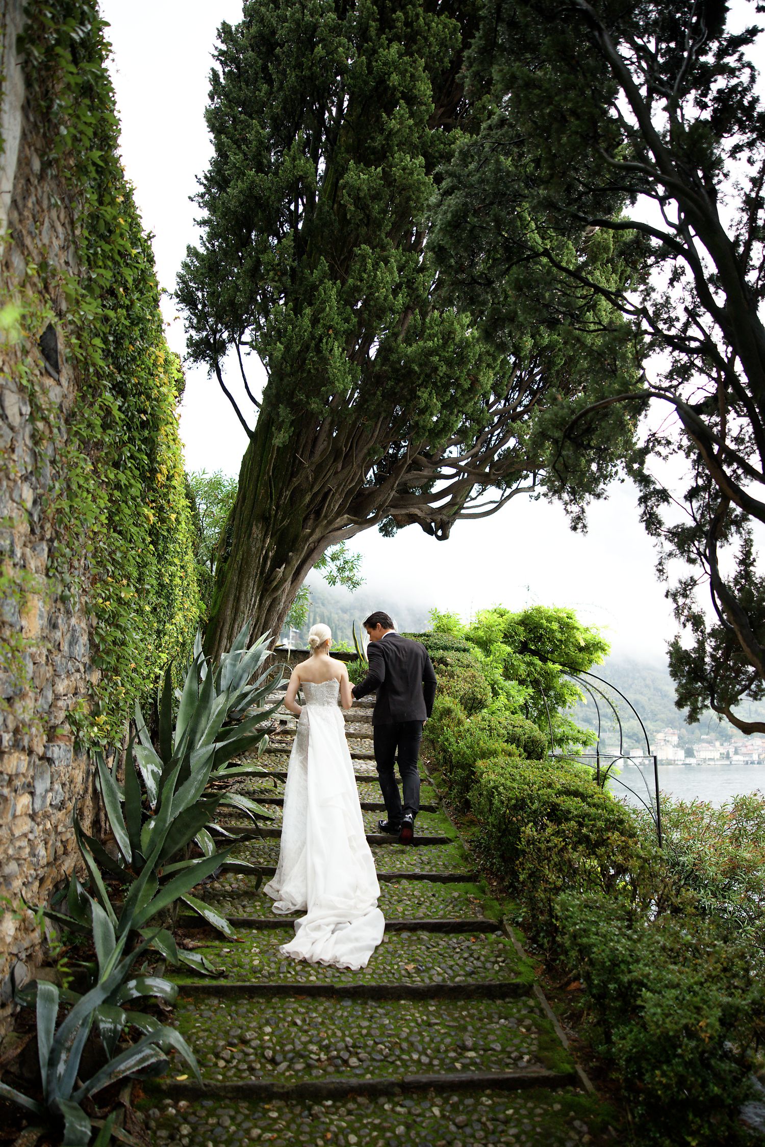 Couple walking up stone garden steps with lush greenery and trees along a beautiful outdoor path.
