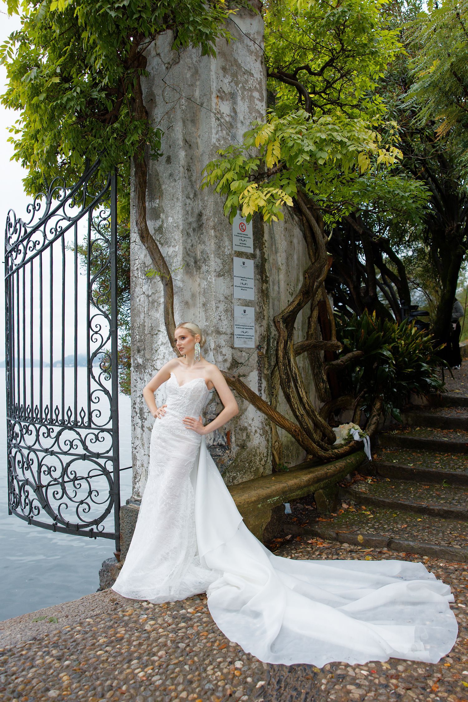 Elegant wedding gown with long train photographed against ornate iron gate and lush garden setting.