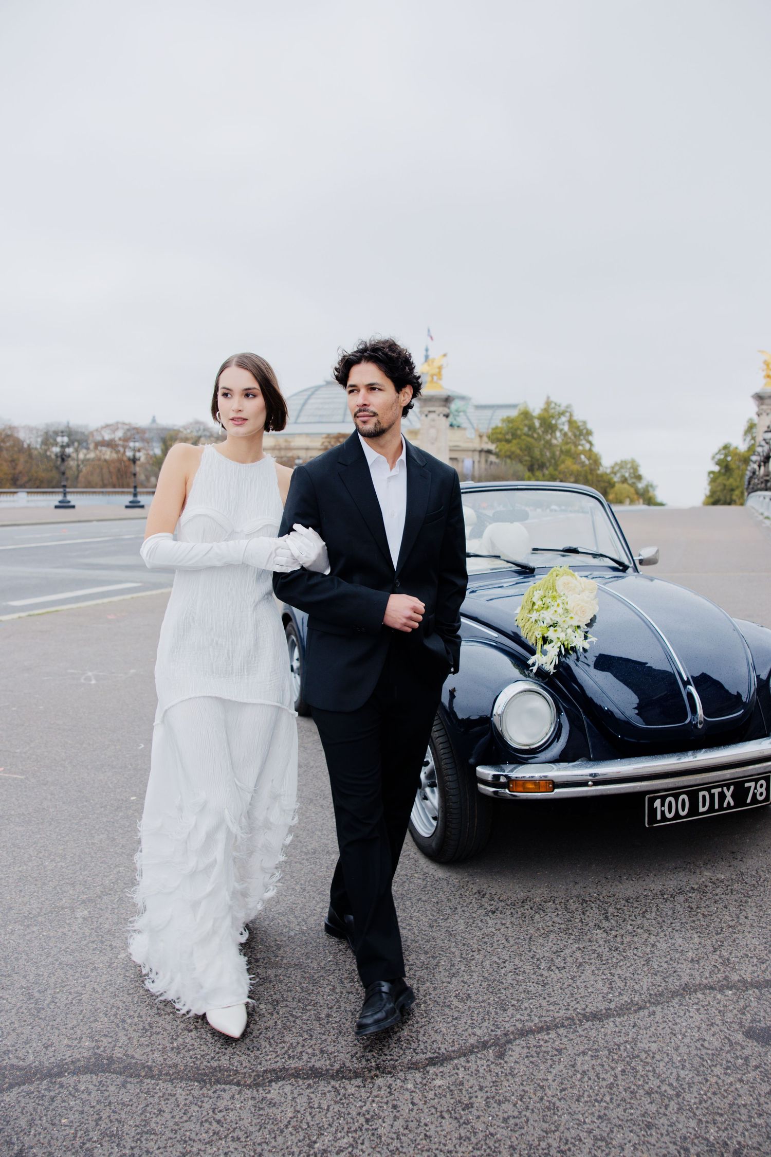 A romantic wedding photo featuring a classic black Volkswagen Beetle decorated with flowers in the background.
