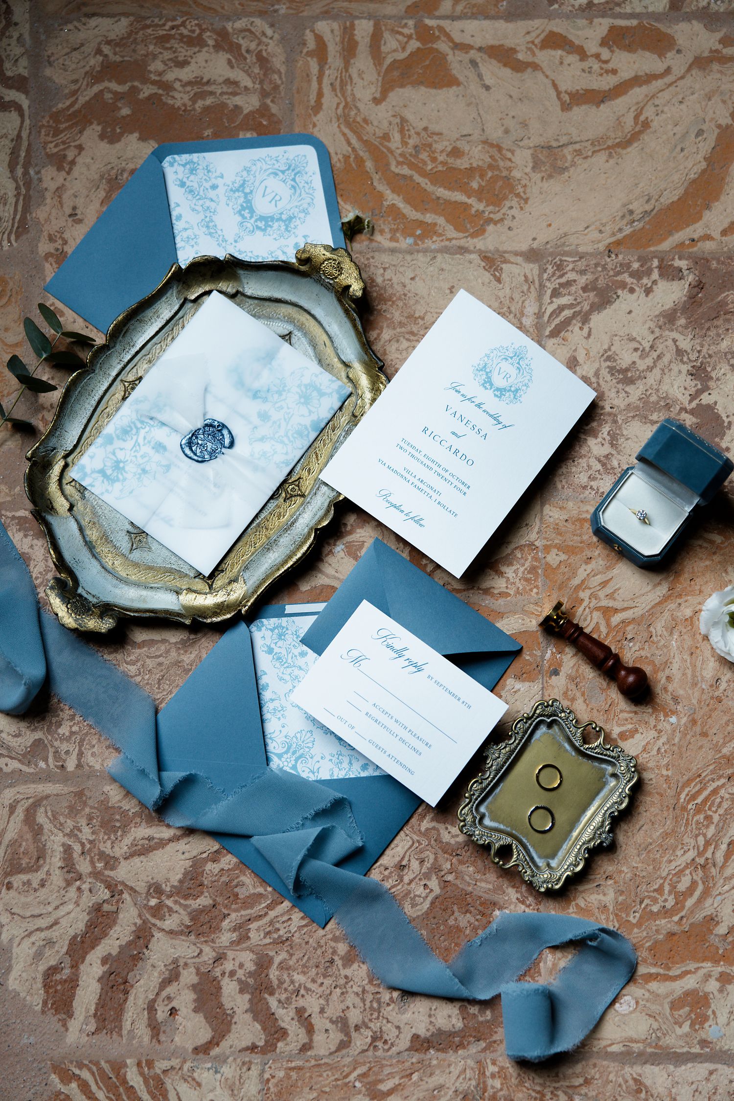 Elegant wedding stationery suite in dusty blue and white featuring ornate trays, ribbons, and invitation cards on marble surface.
