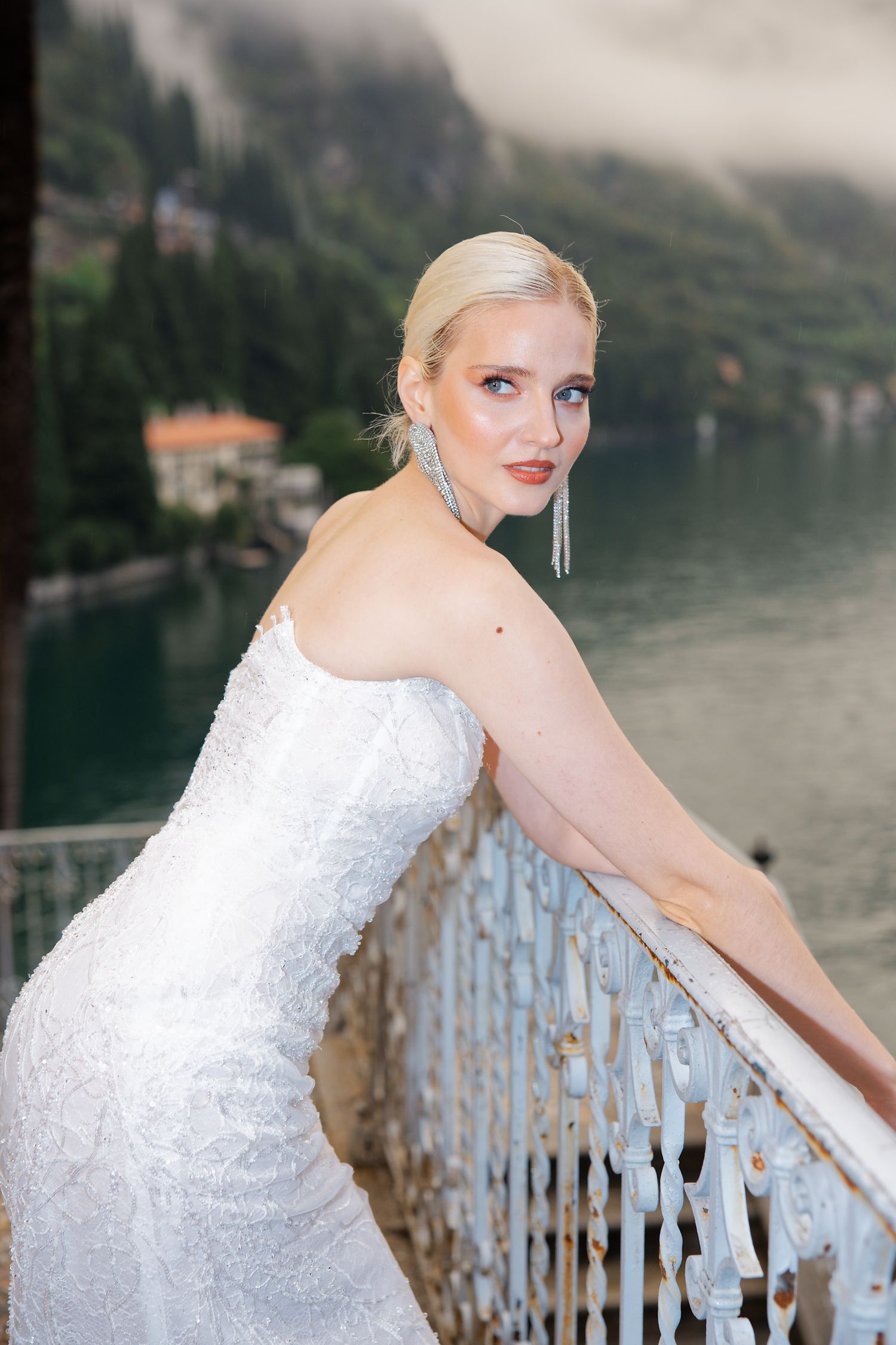 A white lace wedding dress against a scenic lakeside backdrop with mountains and mist.