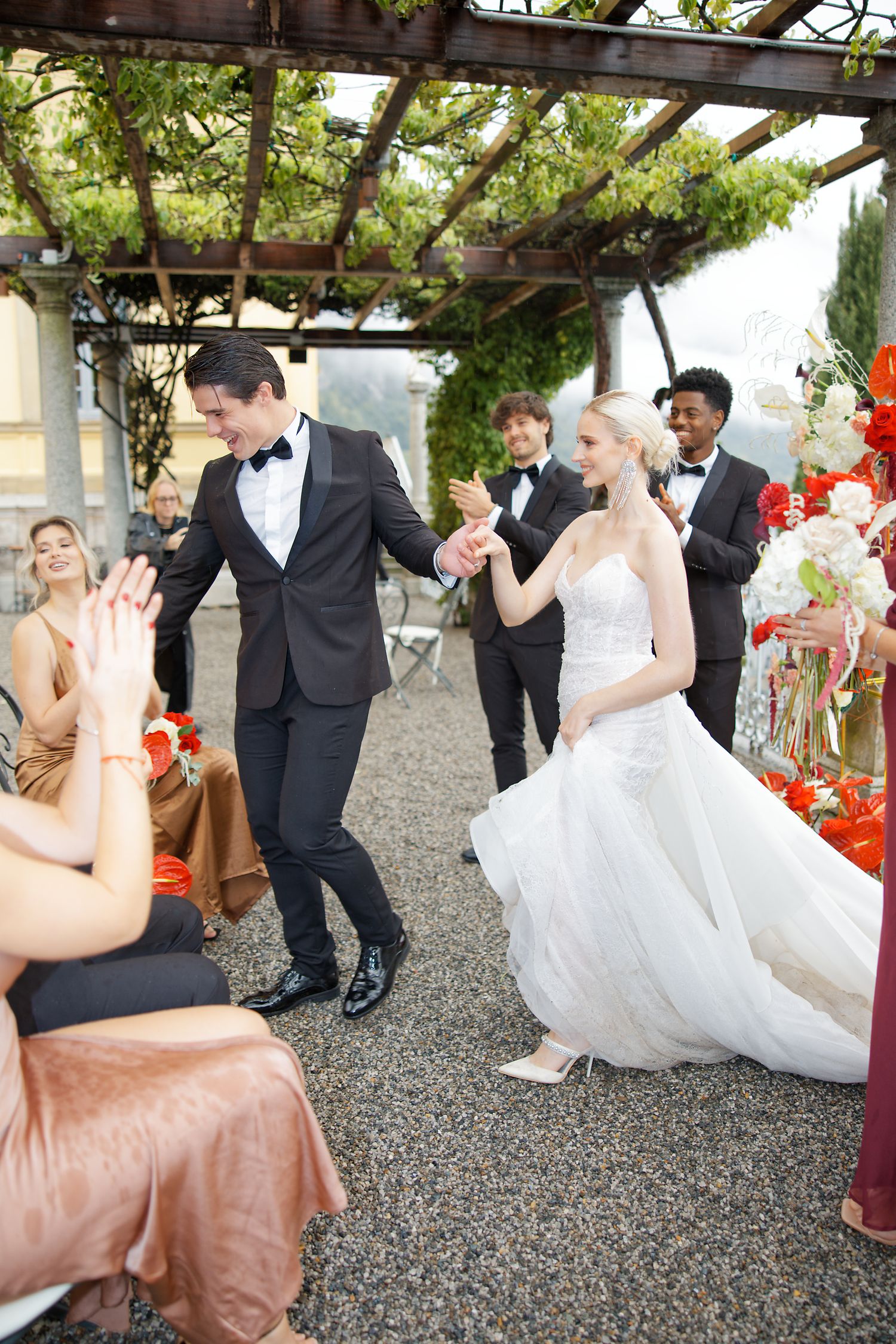 Couple dancing at outdoor wedding reception under vine-covered pergola.