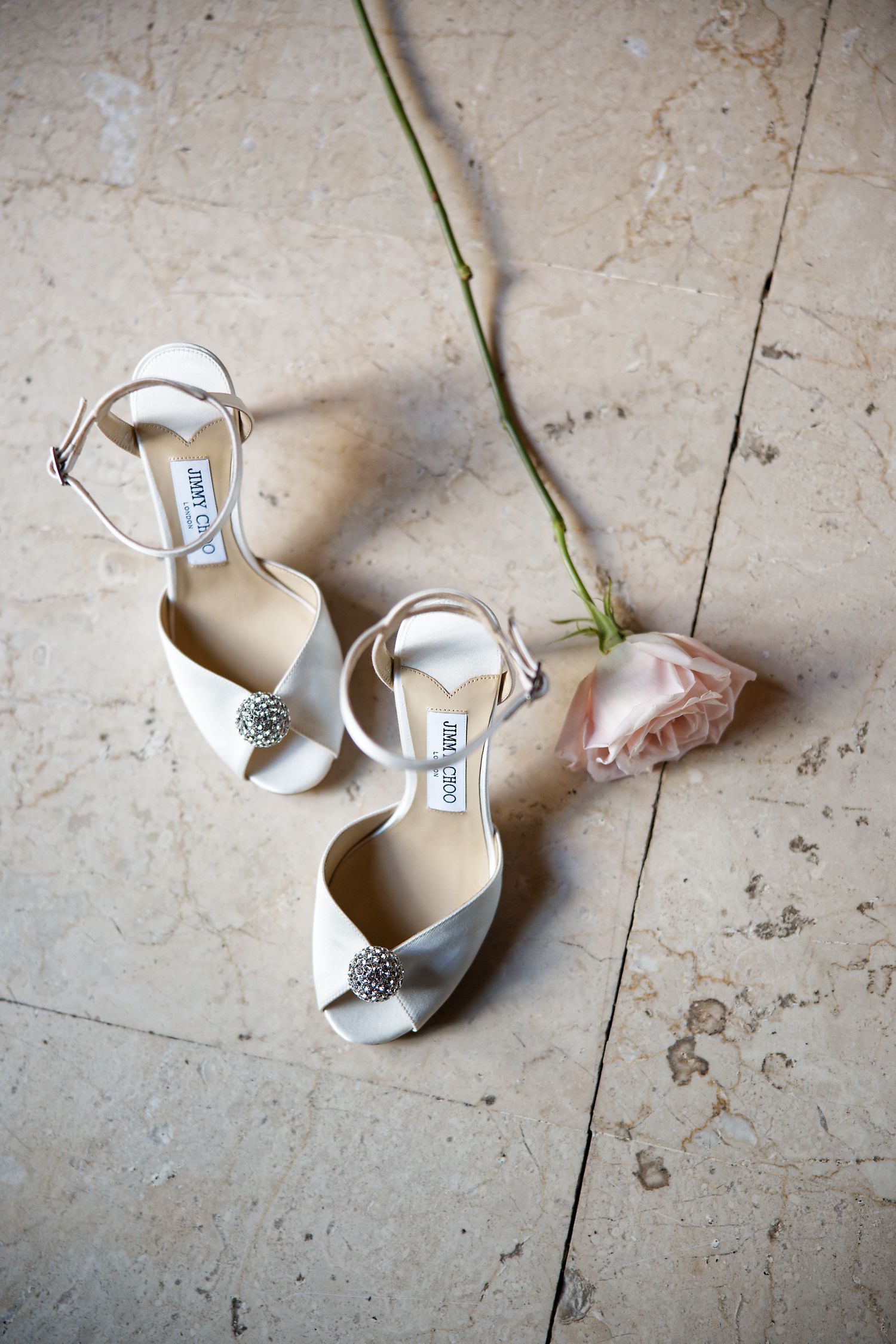 White Jimmy Choo bridal shoes with crystal embellishments displayed with single pink rose.