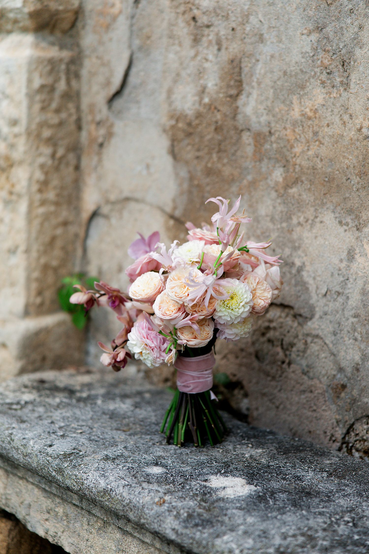 A delicate bridal bouquet with blush roses and pink flowers rests on a weathered stone ledge.