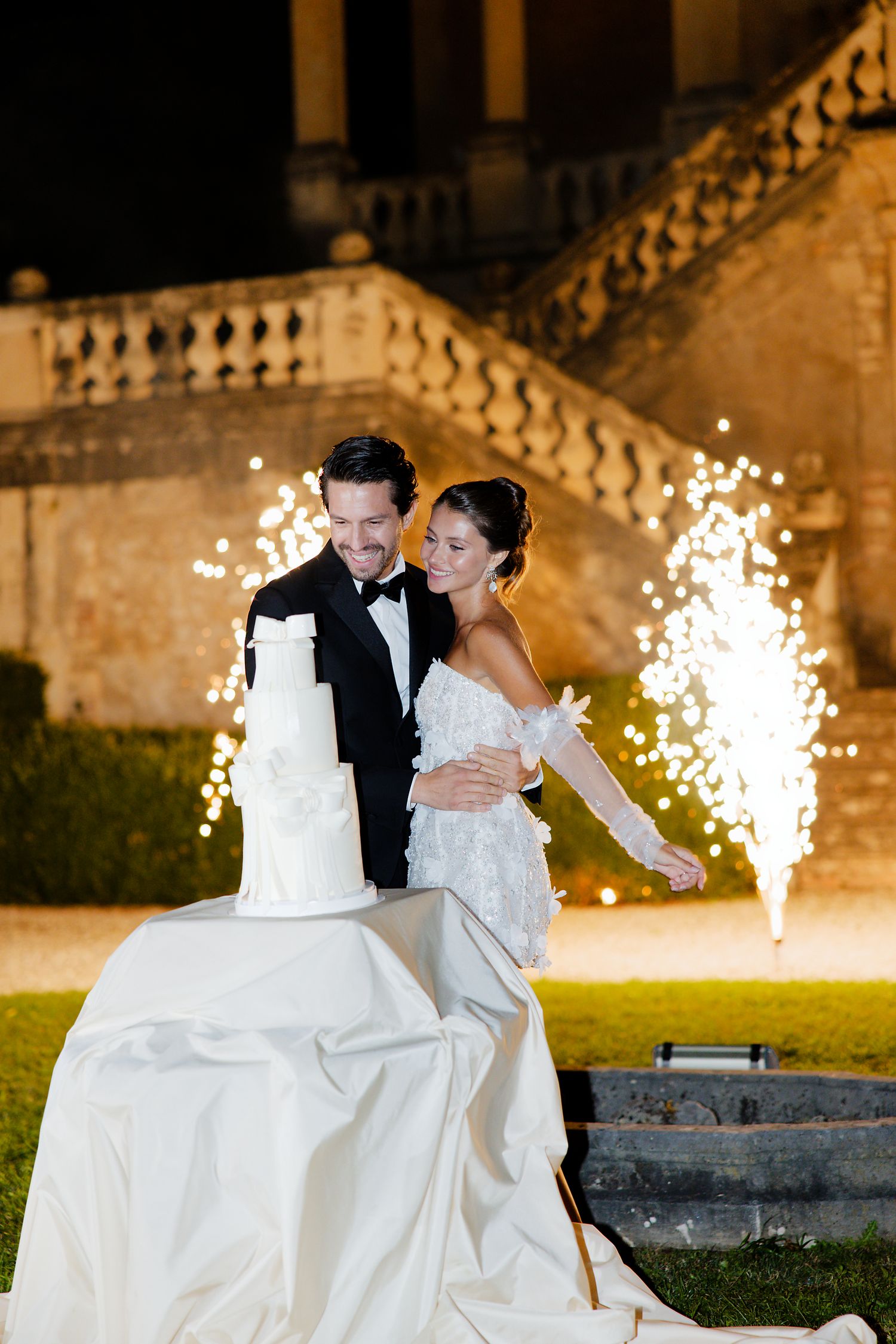 Newlyweds stand by their wedding cake with dramatic sparkler fountains at historic venue.