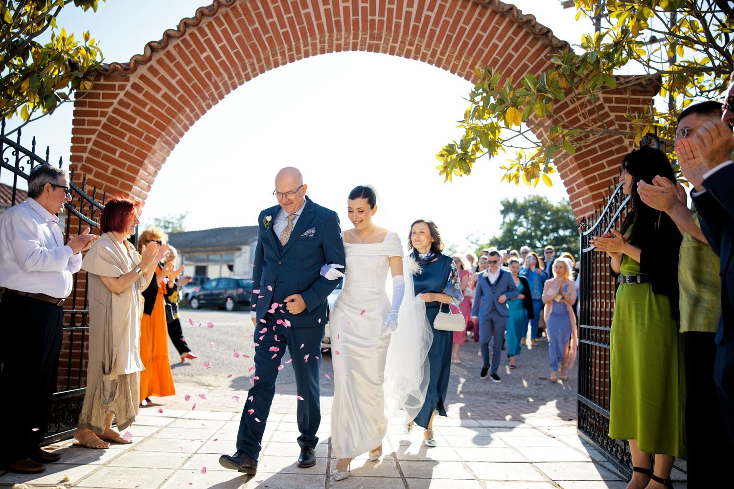 Wedding party exits through brick archway as guests line pathway clapping and celebrating.