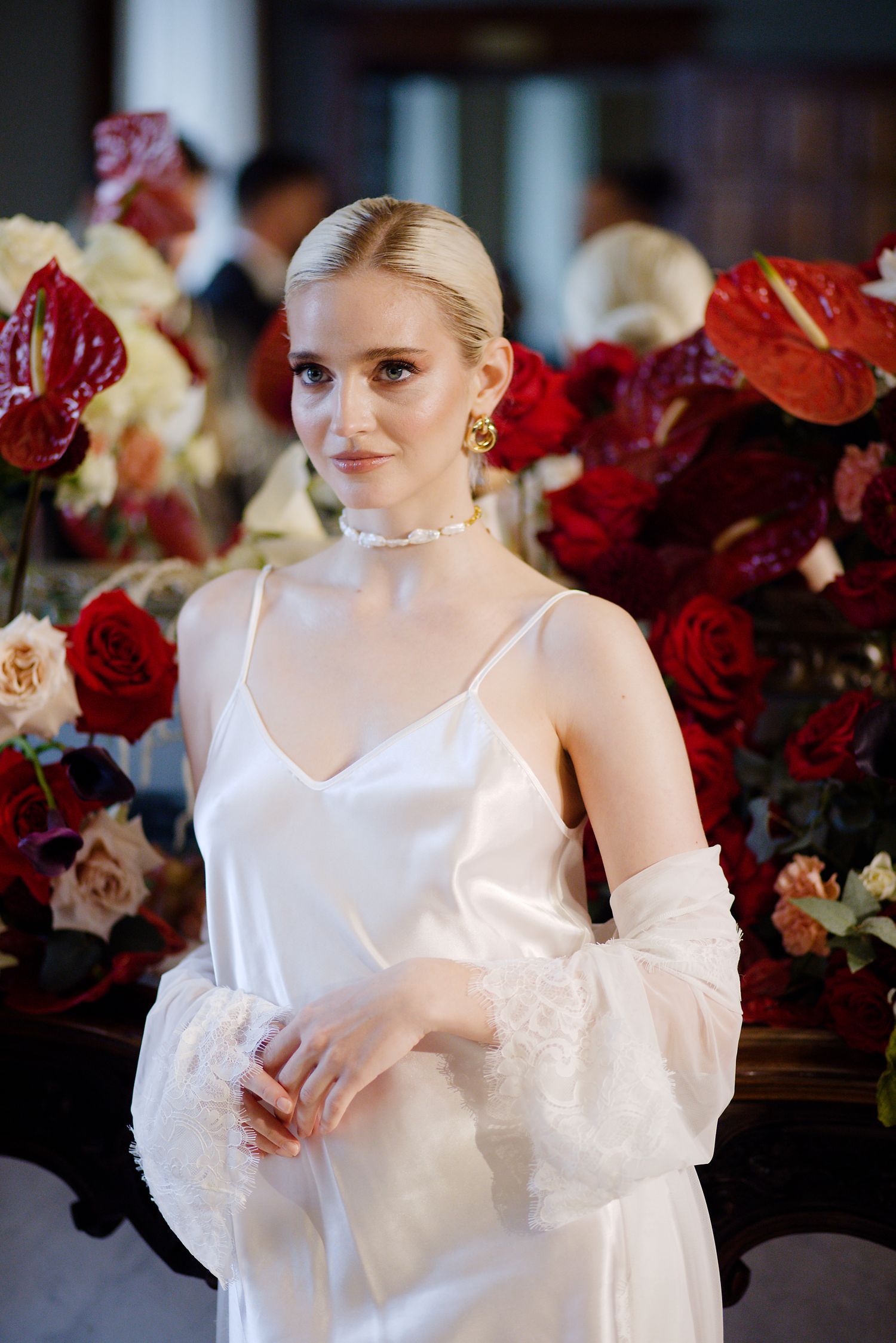 Elegant bridal look featuring silk dress and statement jewelry against backdrop of red roses.