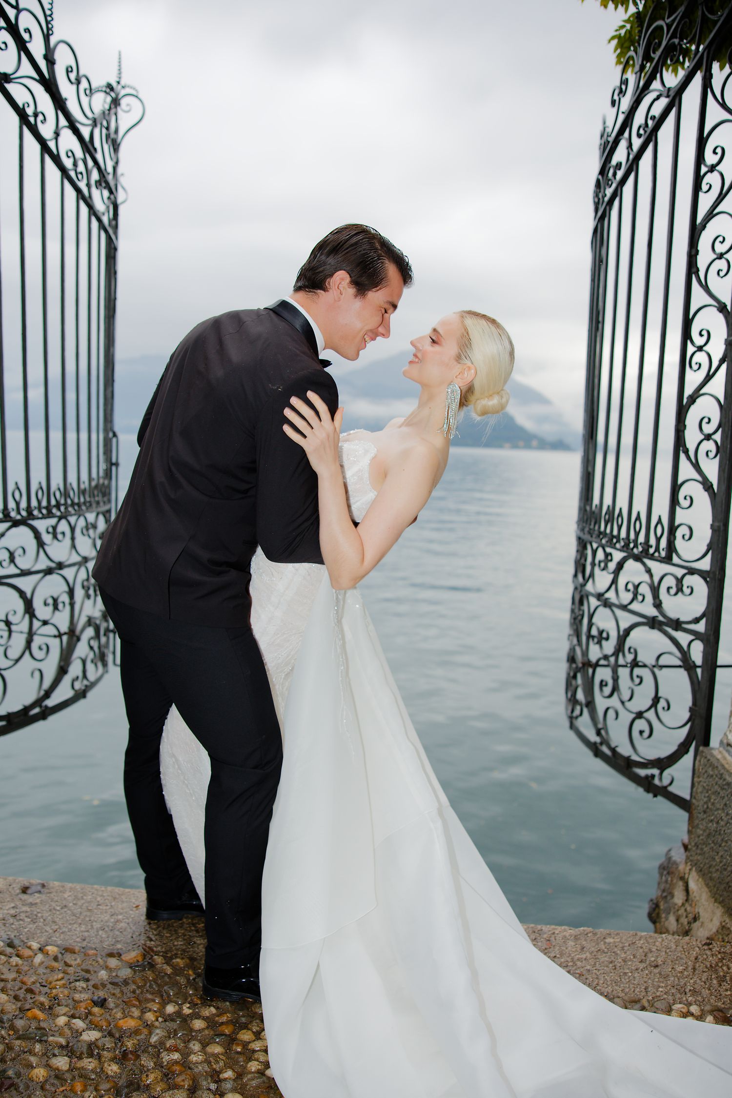 Romantic wedding portrait by ornate iron gates overlooking a misty lake and mountains.