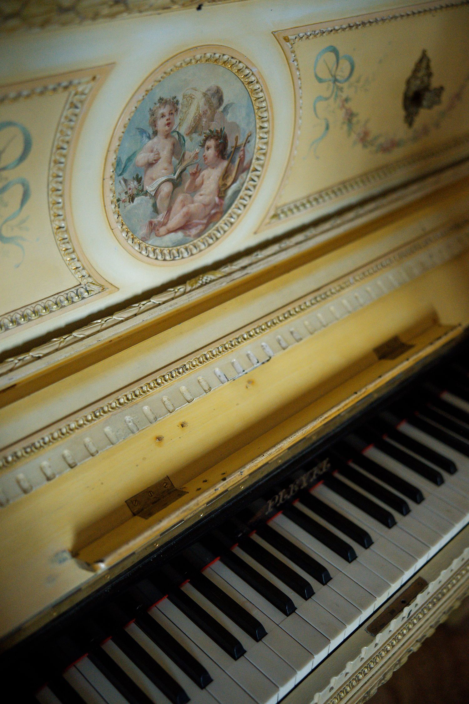 Vintage piano with ornate cherub painting detail on cream colored panel.