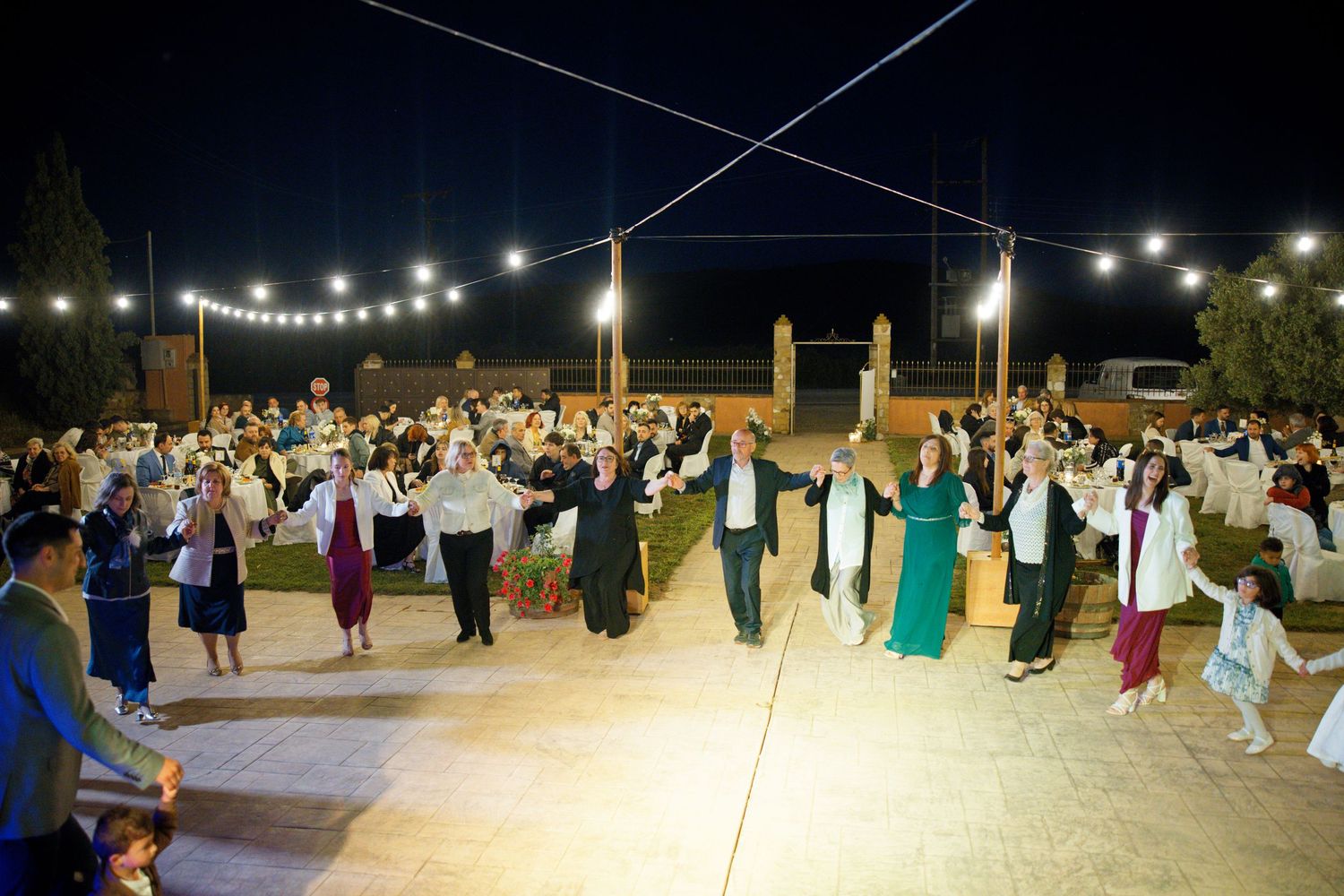 Outdoor evening wedding reception with string lights and guests dancing on a patio.