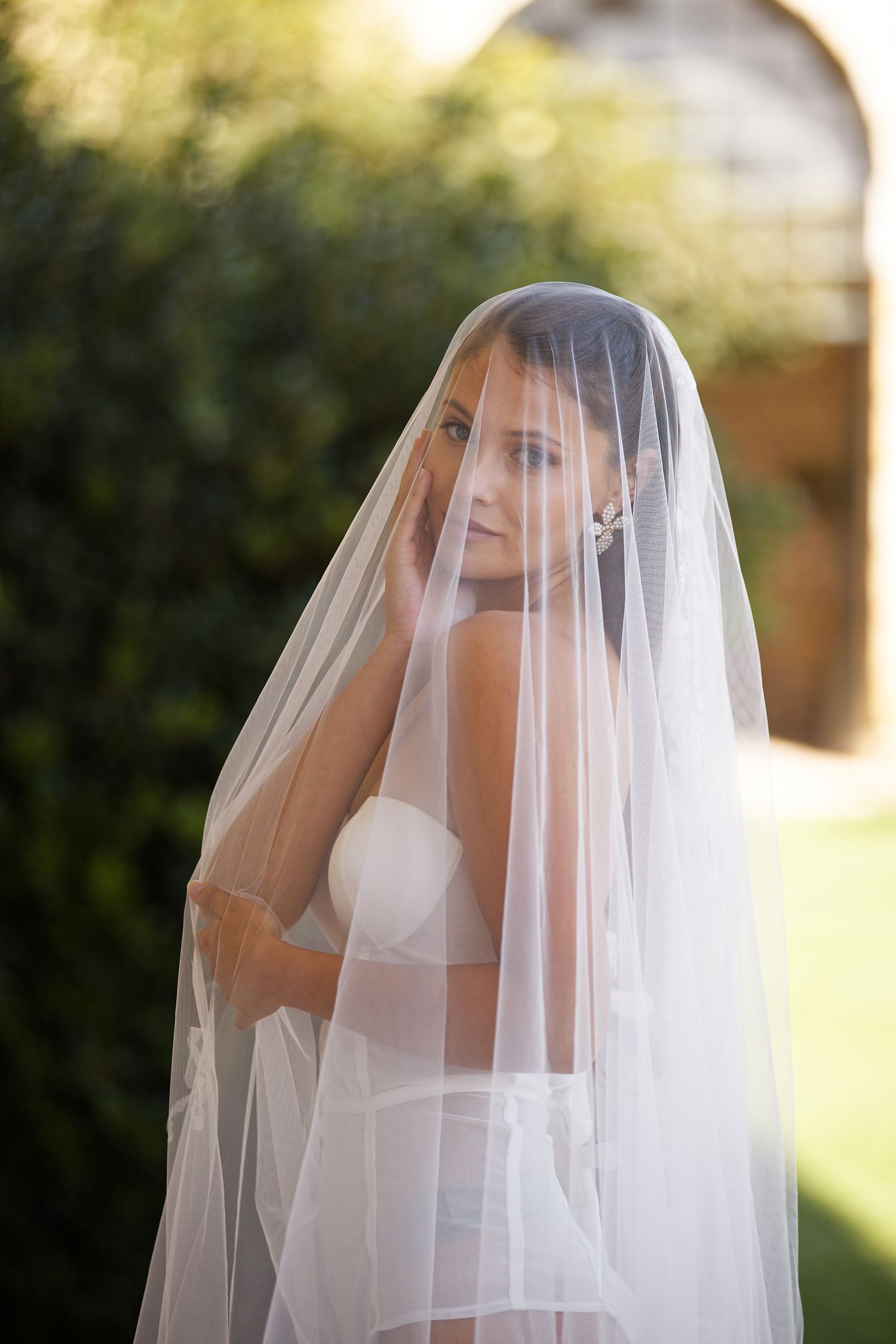 Ethereal bridal portrait showing a flowing white veil in soft natural light against a garden backdrop.