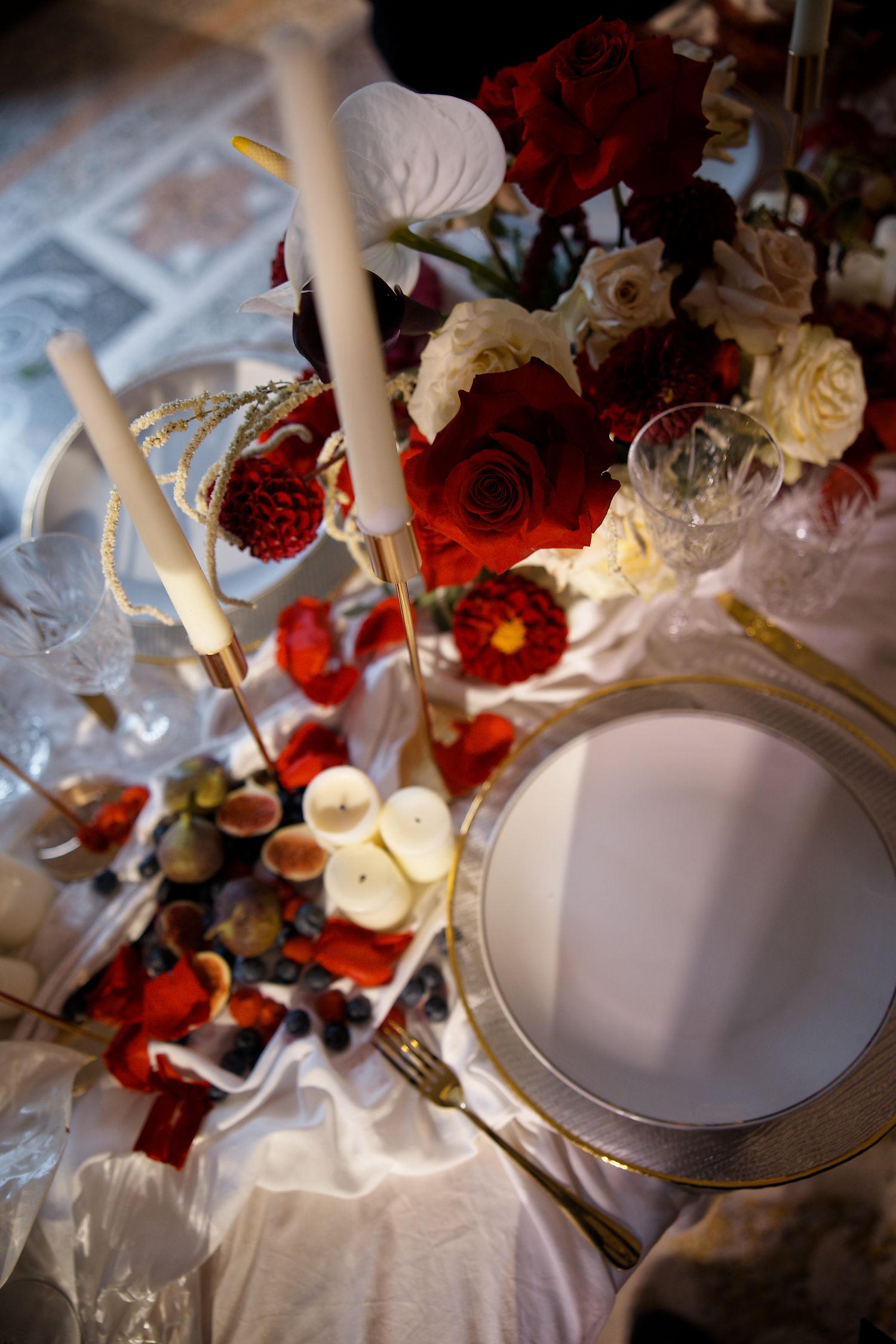 Close-up of luxurious table setting with red roses, white candles and delicate place settings.