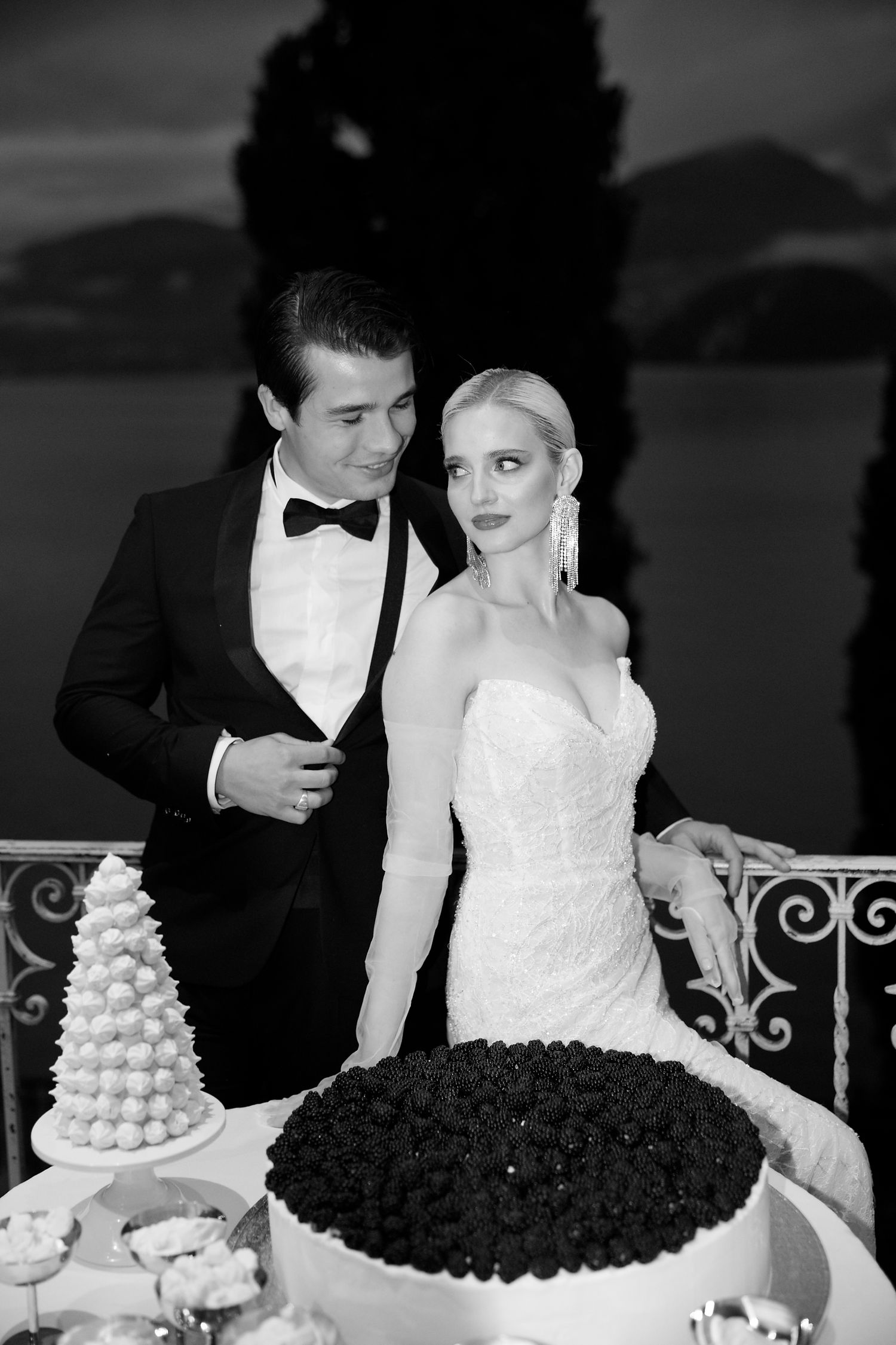 Black and white photo of a bride and groom at their wedding reception with an ornate dessert display on a terrace.