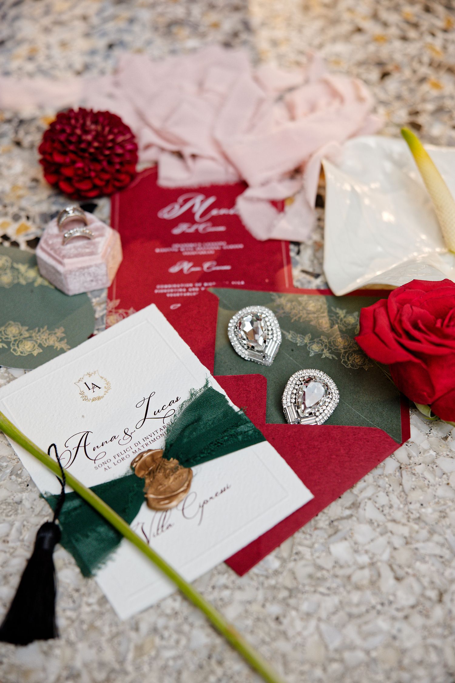 Wedding invitations and details in red and white with wax seals and roses on textured surface.