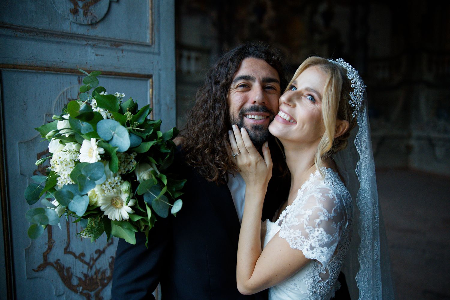 A joyful wedding couple shares a light-hearted moment with white floral bouquet.