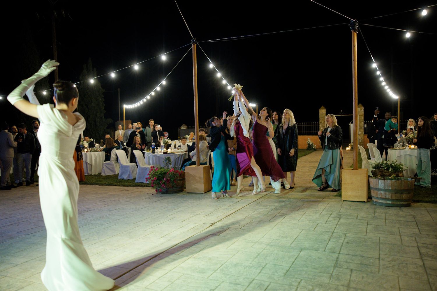 Night wedding celebration showing guests dancing under string lights on an outdoor patio.