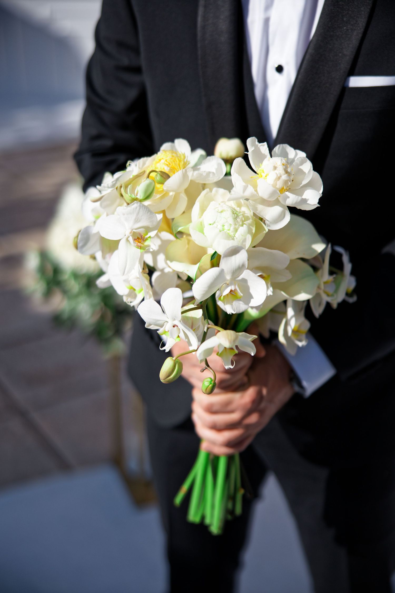 White orchid bouquet held against black tuxedo in wedding photography sequence.