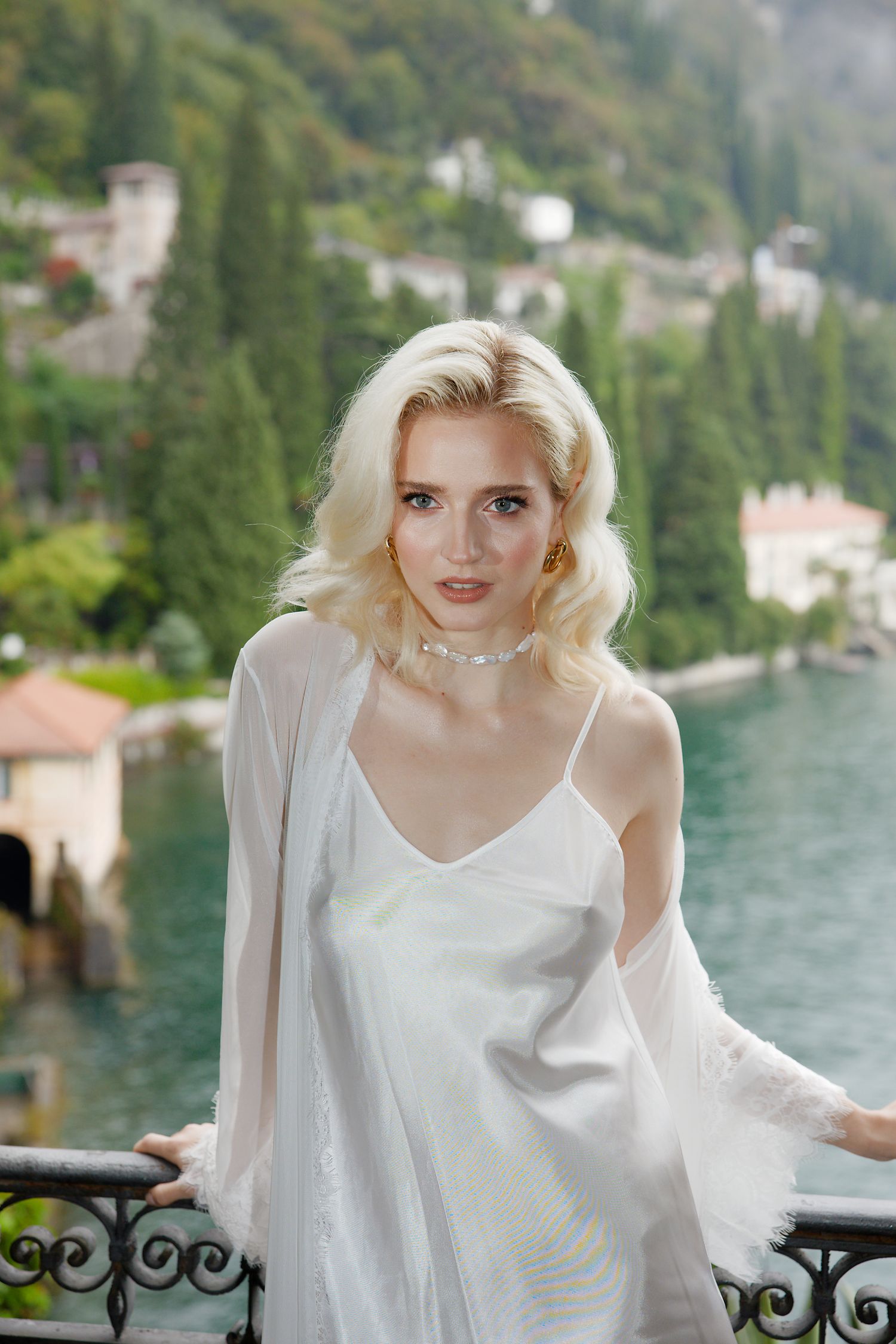Elegant fashion portrait on a balcony overlooking Lake Como with cypress trees and villas.