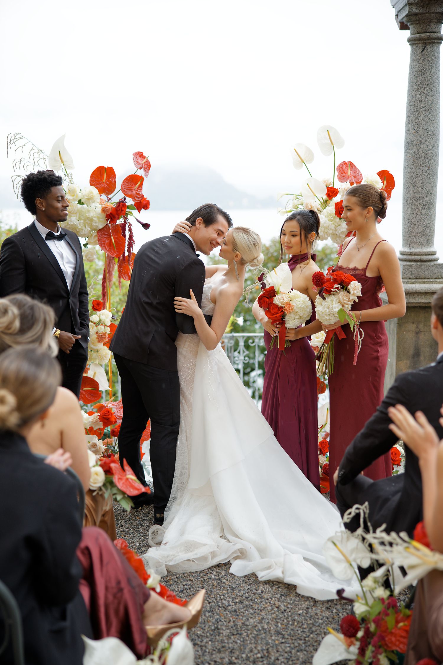 Wedding ceremony on a terrace with red floral arrangements and burgundy bridesmaid dresses.