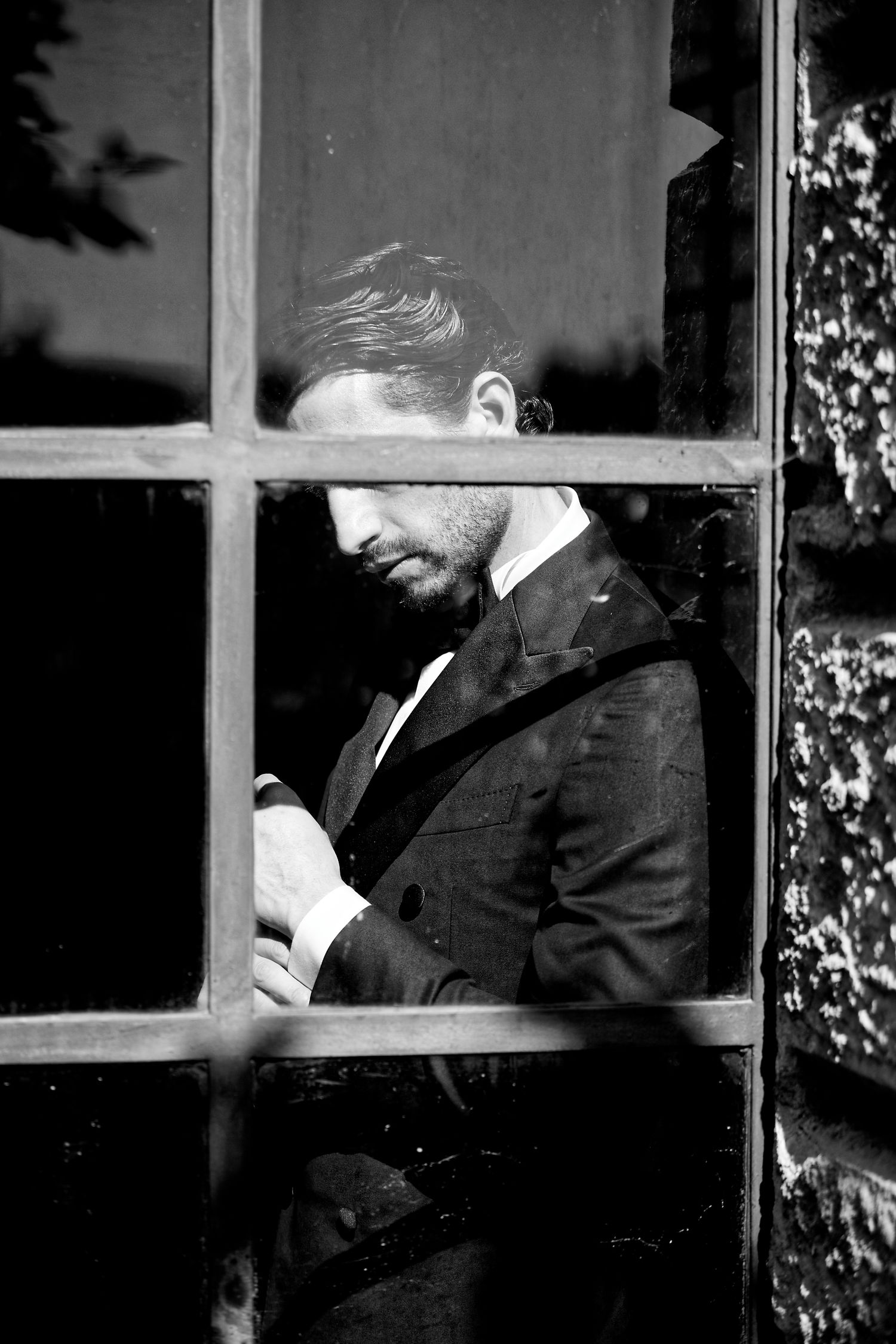 Artistic black and white portrait of a groom seen through a window pane.