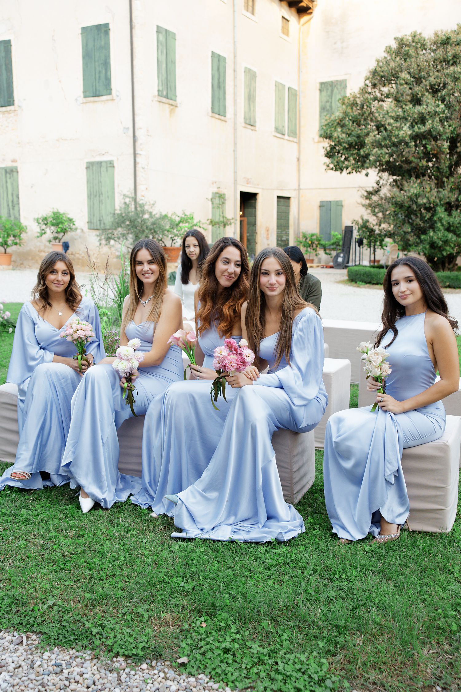 Bridesmaids in flowing powder blue dresses pose together on a lawn outside an elegant venue.