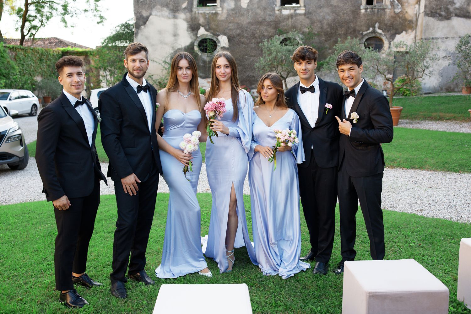 Wedding party in formal attire posing together outside historic venue with bridesmaids in light blue dresses.
