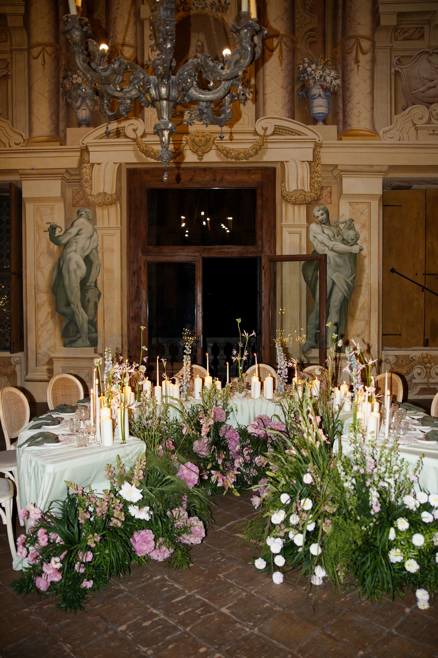 Luxurious wedding reception table with floral centerpieces and candles in an ornate classical room.