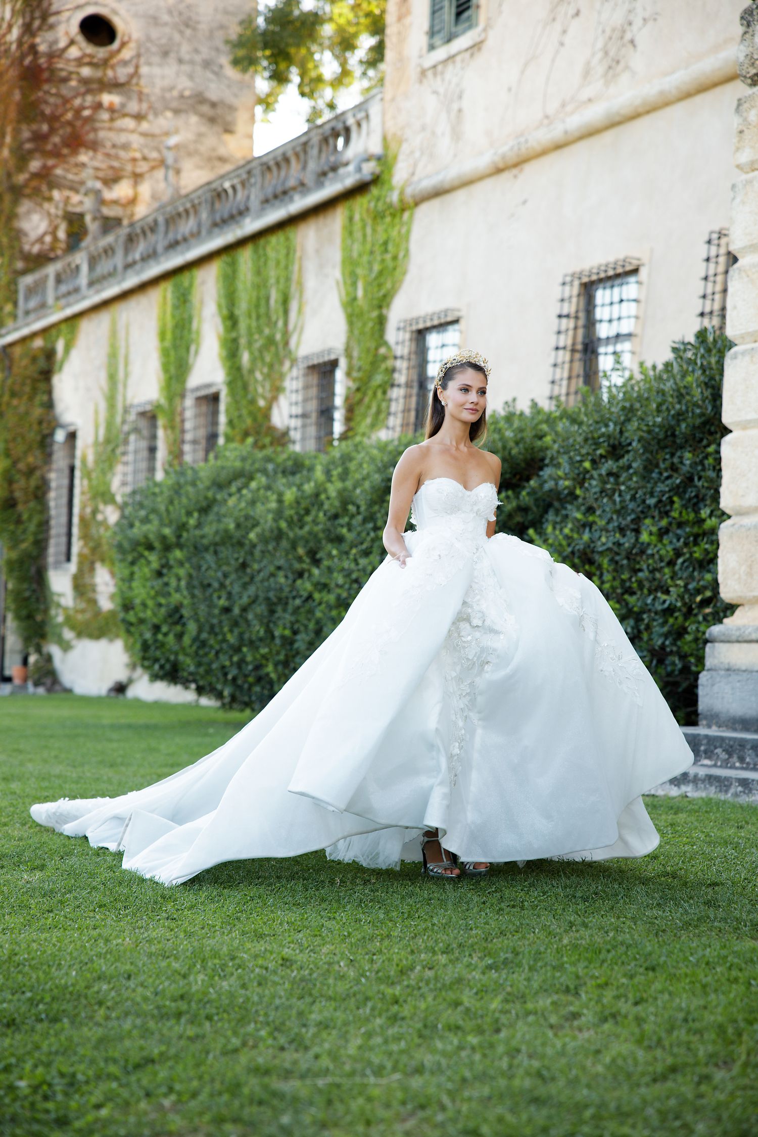 A flowing white wedding gown with sweetheart neckline photographed in front of an ivy-covered historic building.