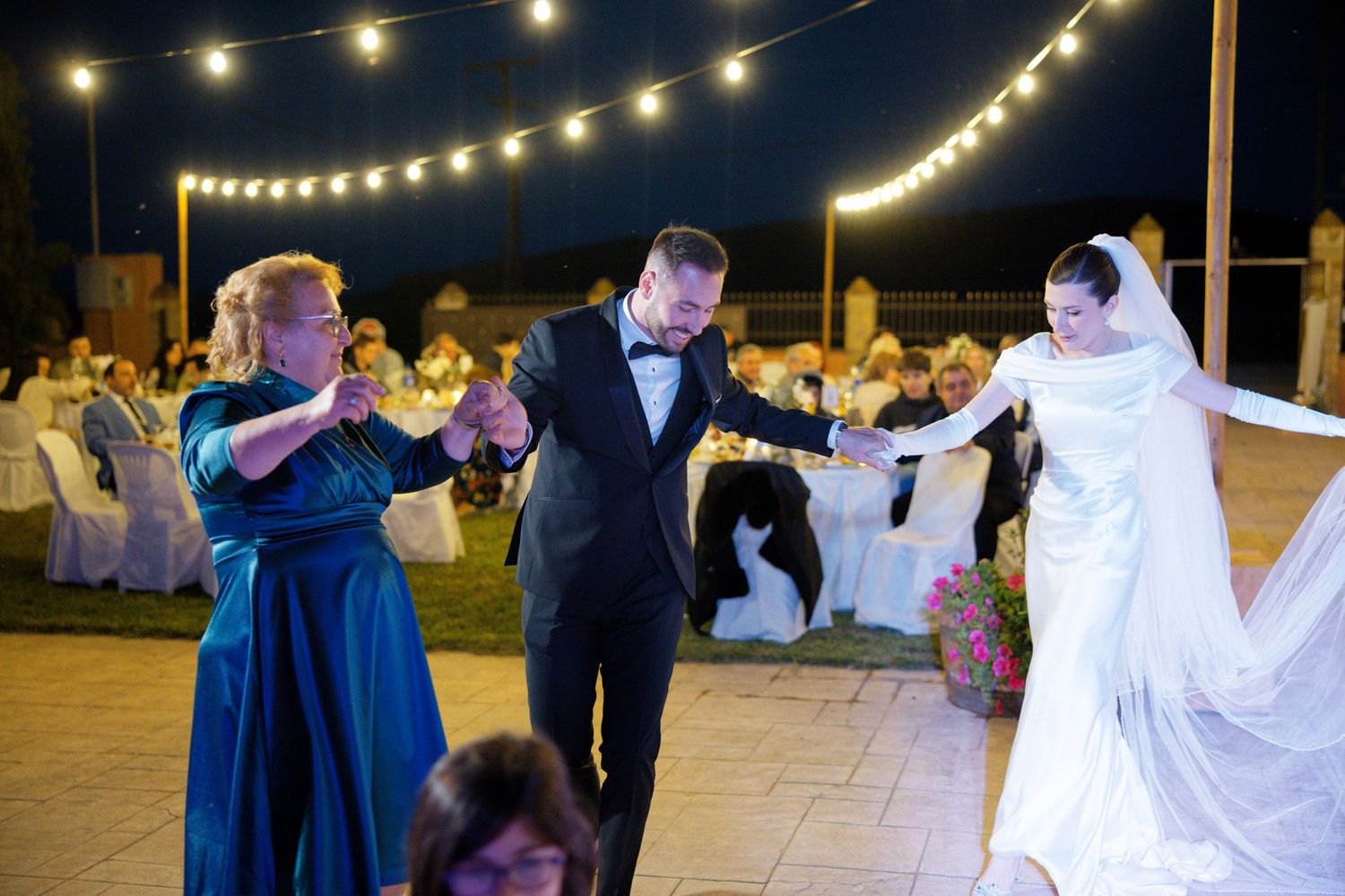 Wedding celebration with dancing guests under string lights at an outdoor reception.