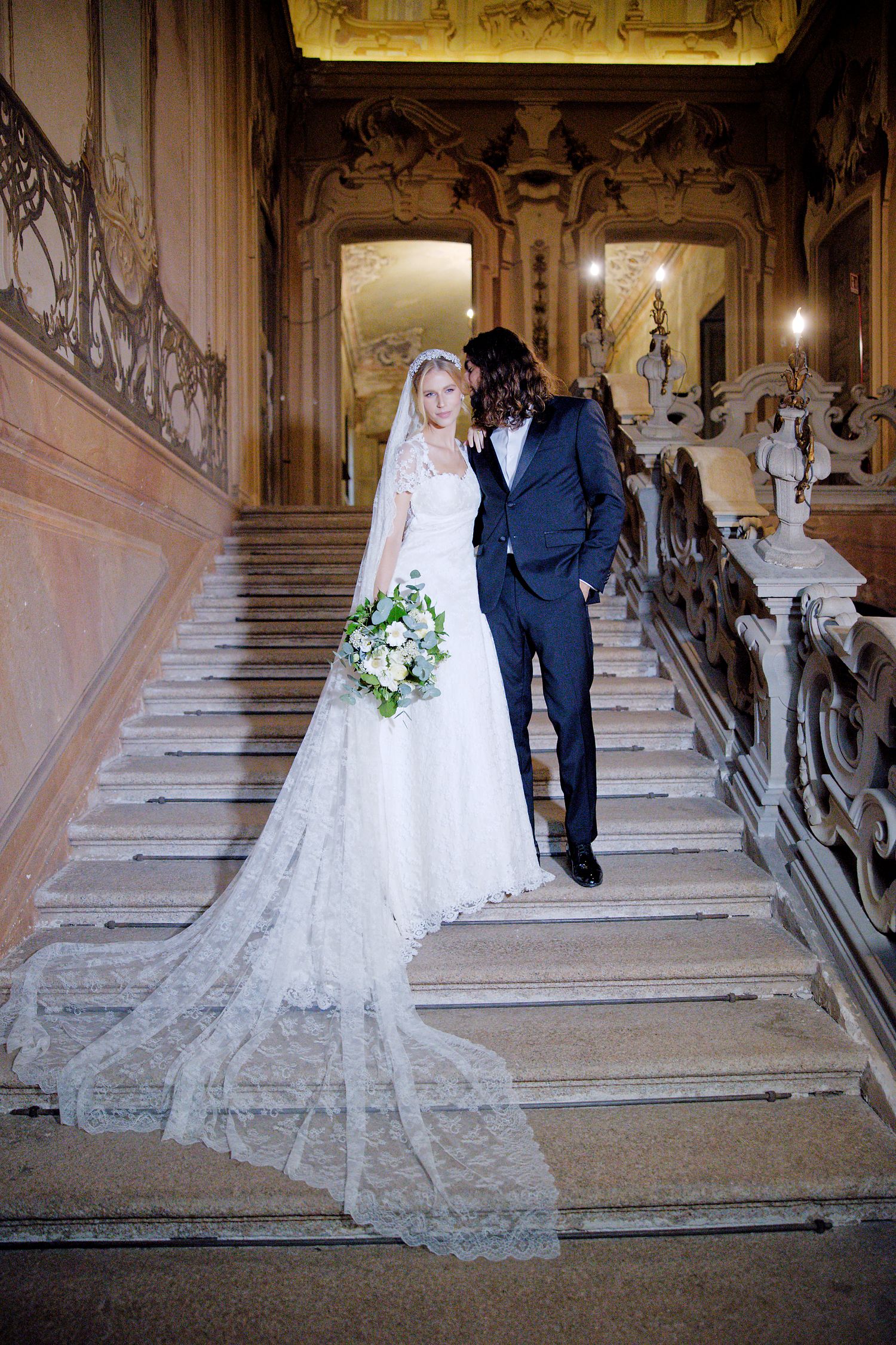 Elegant couple sharing an intimate moment on a grand baroque staircase with intricate architectural details.