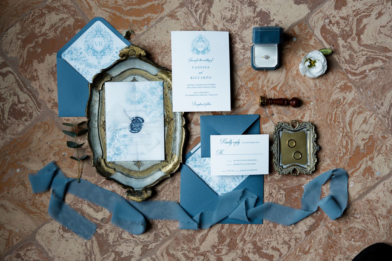 Wedding stationery suite in dusty blue and white with vintage frames and silk ribbons laid on marble surface.
