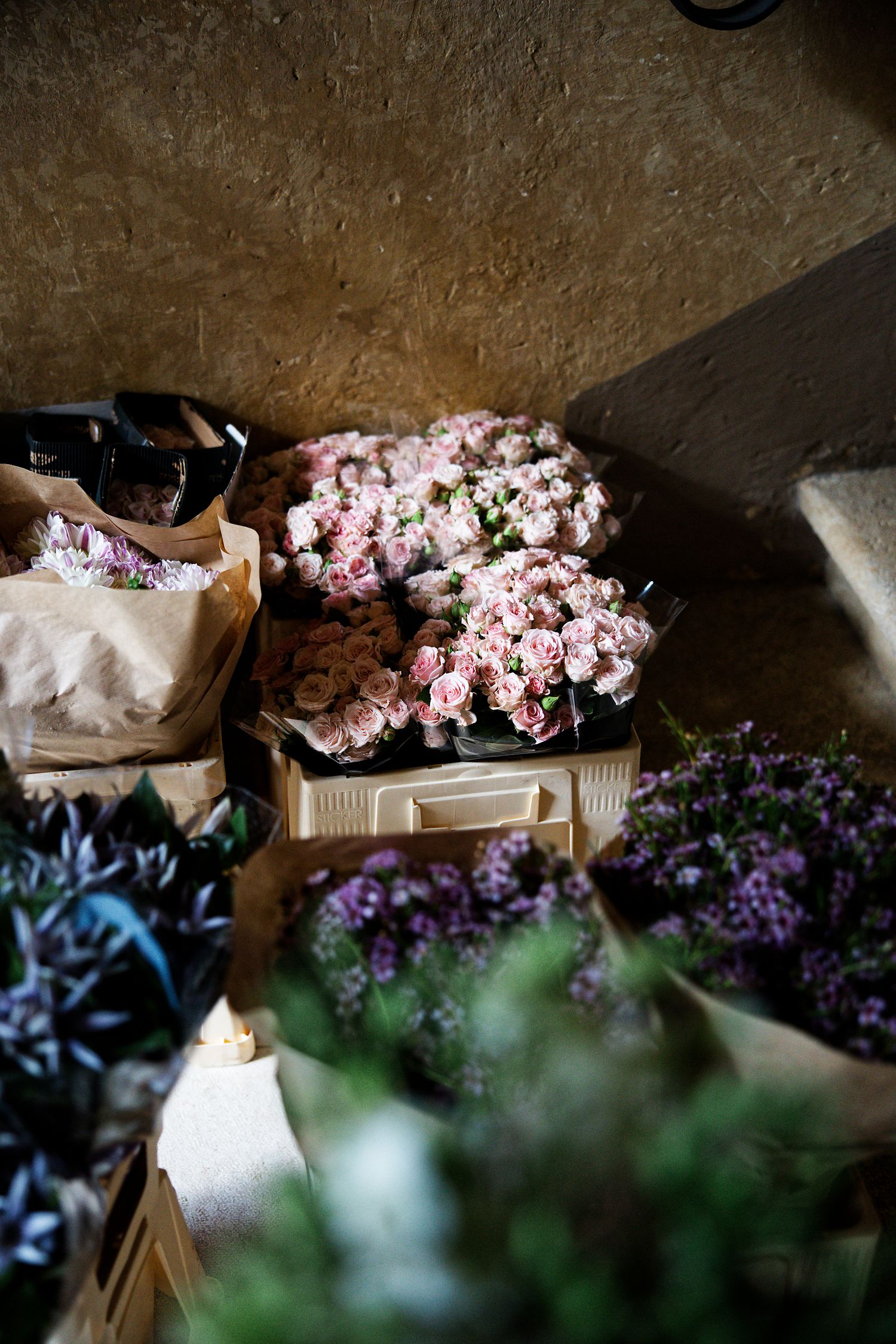 Fresh pink and purple flowers arranged in rustic wooden crates in a dimly lit space.