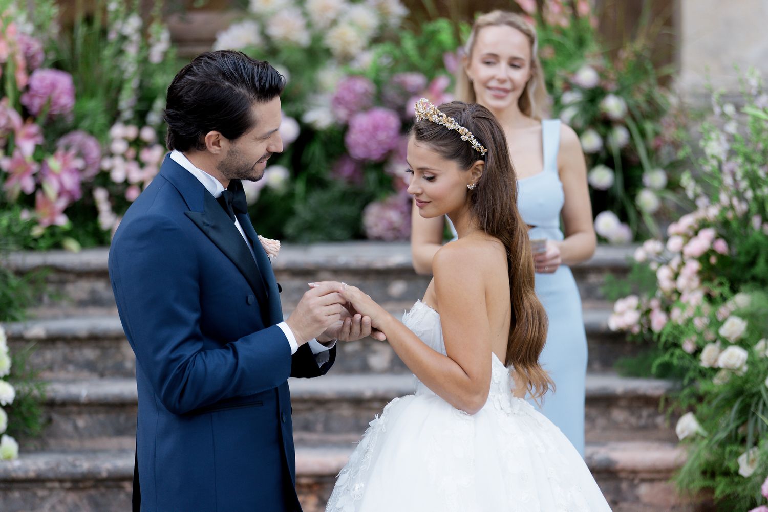 Romantic moment captured on garden staircase surrounded by pink flowers and classical architecture.