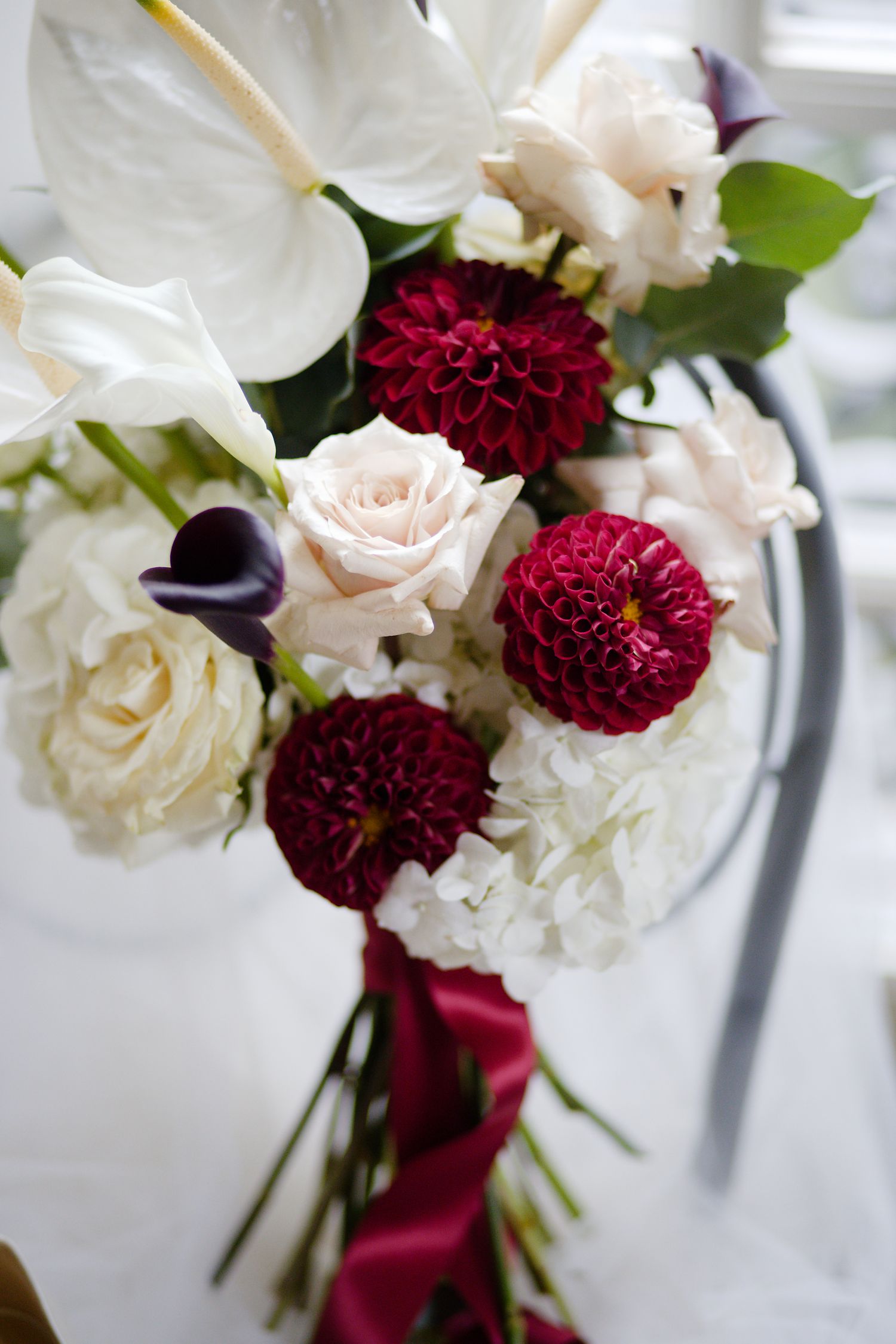 Elegant bridal bouquet with white anthuriums, burgundy dahlias, and cream roses.